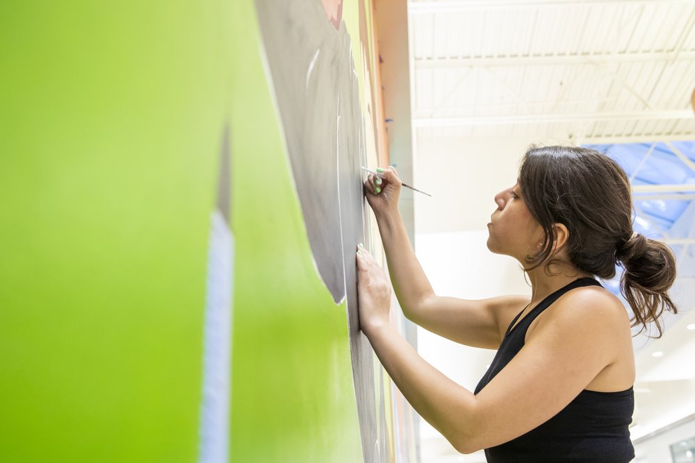  Carina Santillan, GMU Alum, paints mural at Manassas Mall. Photo by:  Sierra Guard/Creative Services/George Mason University 