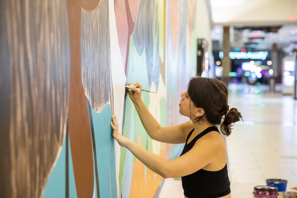  Carina Santillan, GMU Alum, paints mural at Manassas Mall. Photo by:  Sierra Guard/Creative Services/George Mason University 