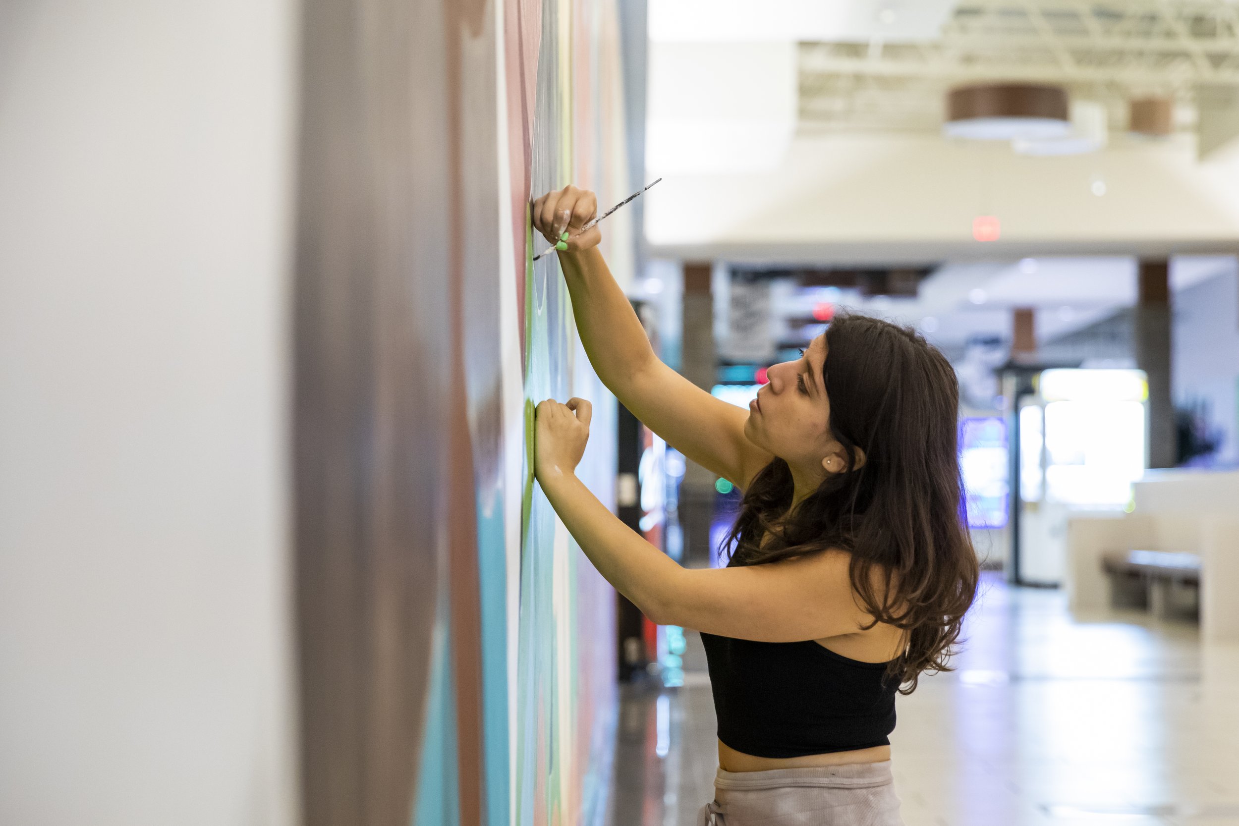  Carina Santillan, GMU Alum, paints mural at Manassas Mall. Photo by:  Sierra Guard/Creative Services/George Mason University 