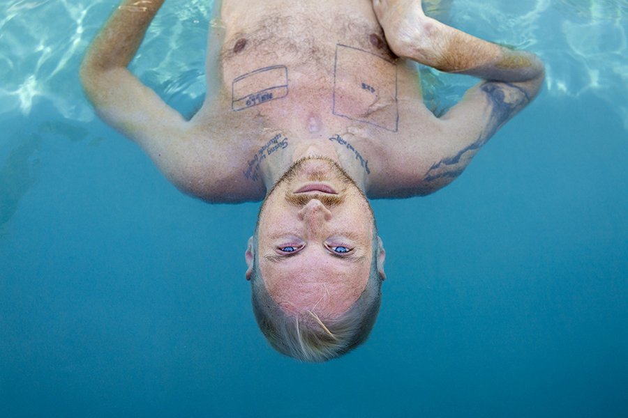    Eyes Blue like the Atlantic   ,  2022 Digital pigment print on Slickrock Metallic Pearl 260 paper 40 x 60 inches  Robert, a white man white short blonde hair and a goatee is looking at the camera upside down, pictured from the chest up, floating i
