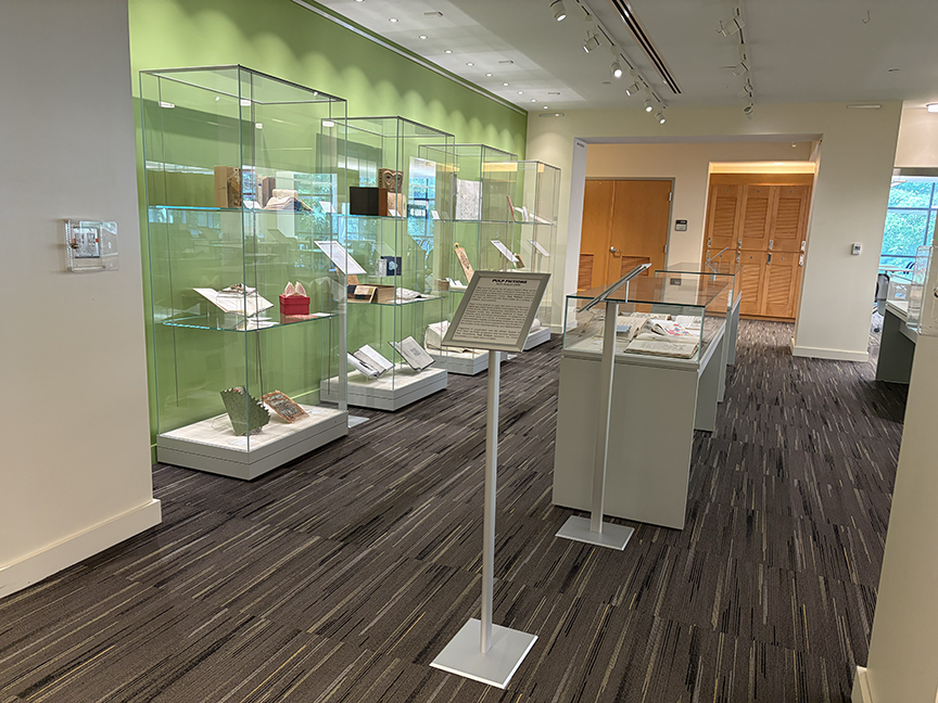 A gallery with gleaming glass cases and a green wall. The cases are filled with small book-like objects.