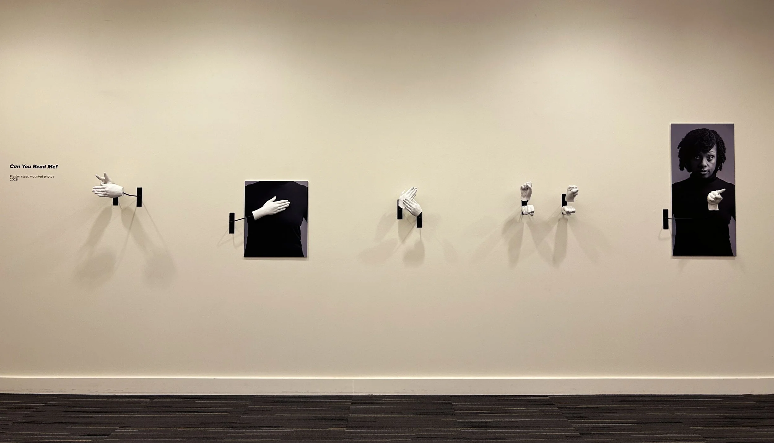 A series of white plaster-cast hands spelling out the phrase "Can You Read Me?" in american sign language. Two of the  casts are backed by photographs of a young Black woman to provide body positioning for the signs.