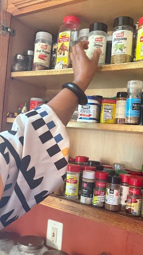 A hand reaches into a well-worn spice cabinet, capturing an intimate moment of daily ritual where memory, flavor, and care are quietly stored side by side.