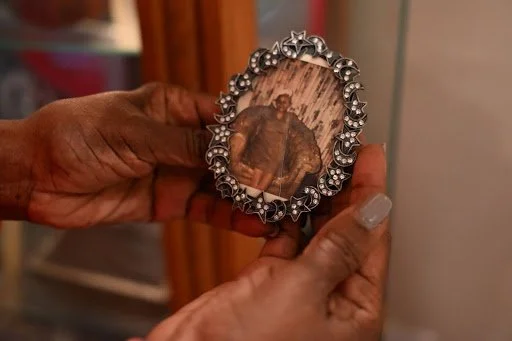 Hands cradle a small, ornate frame, preserving a faded portrait as a tender relic—an intimate gesture where memory, care, and lineage quietly converge.