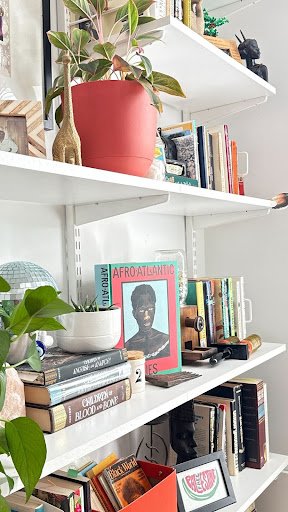 A curated shelf becomes a quiet portrait of identity and memory, where books, plants, and sculptural objects converse across generations and cultures.