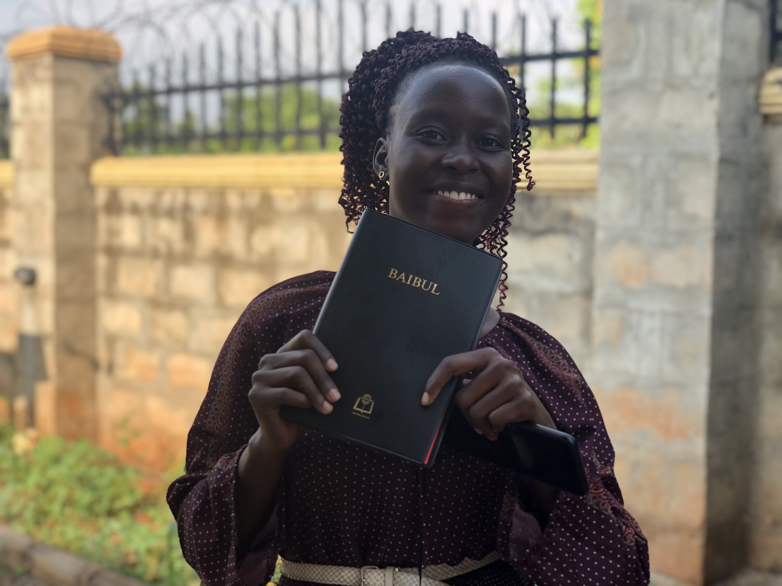Church youth, Babra holding up her first Acholi Bible given as a Christmas gift from TWCC