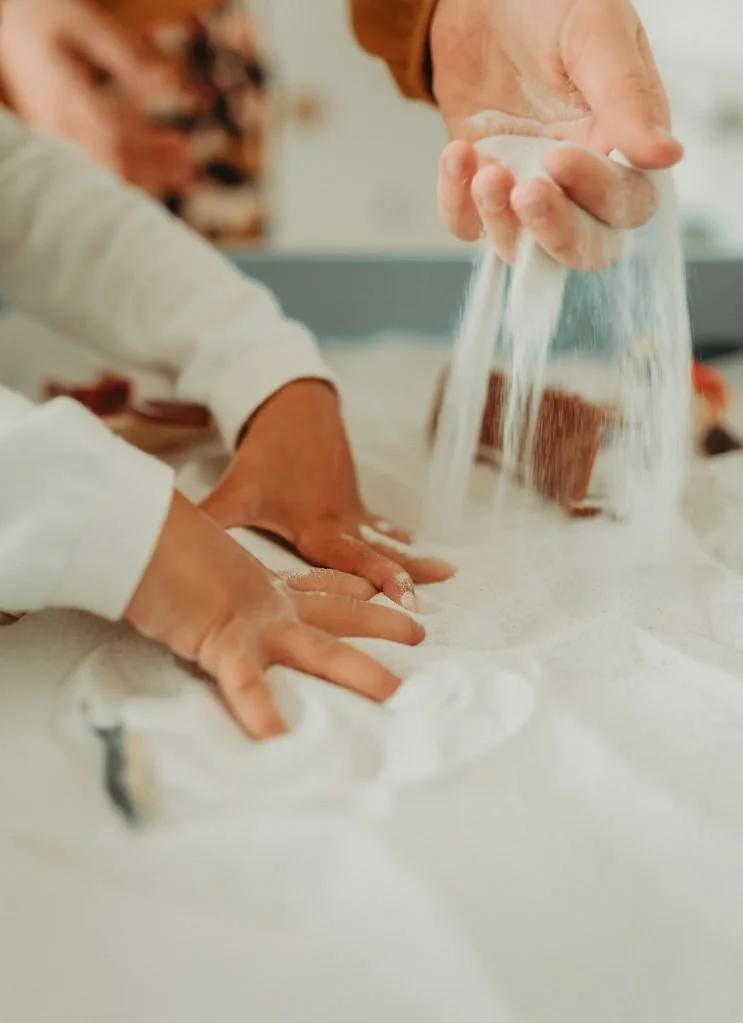 A person sprinkling sand over a toddlers hand