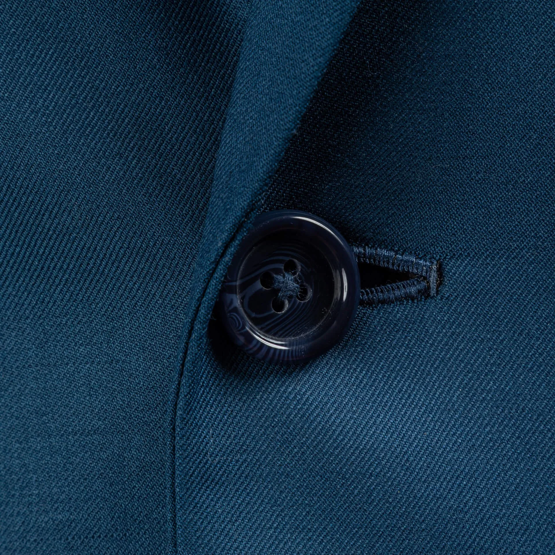 Close-up van donkerblauwe hoornknoop met handgenaaid knoopsgat op petrol blauw bespoke colbert