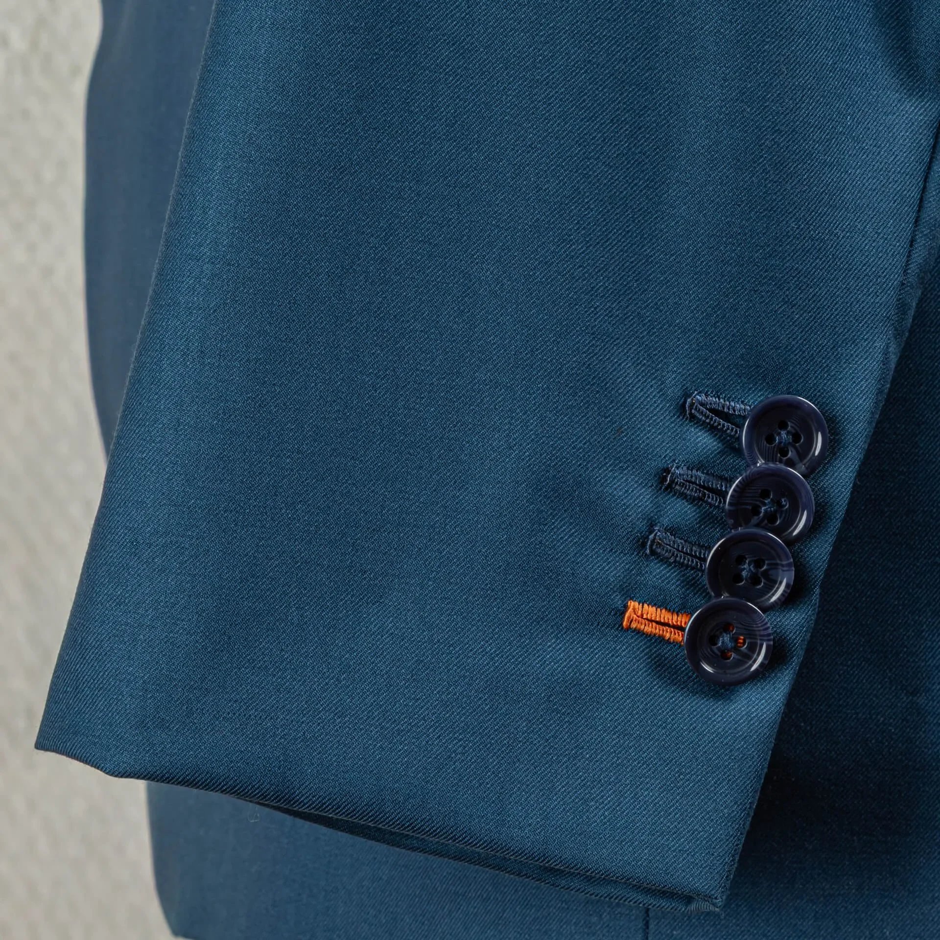 Detail van vier werkende knoopsgaten op mouwsplit met oranje accent knoopsgat, kenmerk van bespoke maatwerk