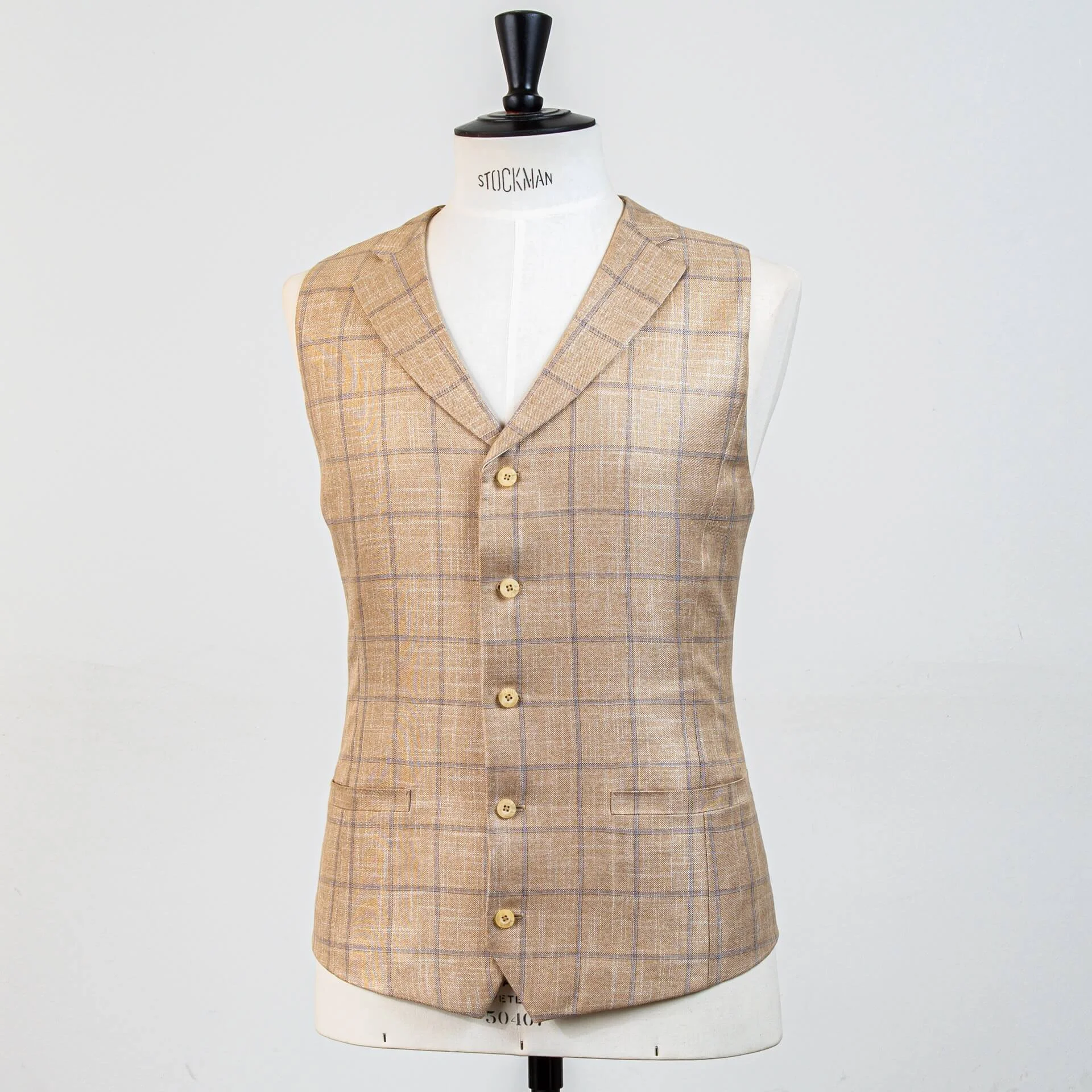 Volledig vooraanzicht zandkleurig bespoke gilet met subtiel blauw windowpane ruit. Single-breasted model met 5 hoornen knopen en notch revers, perfect bij groen trouwpak.