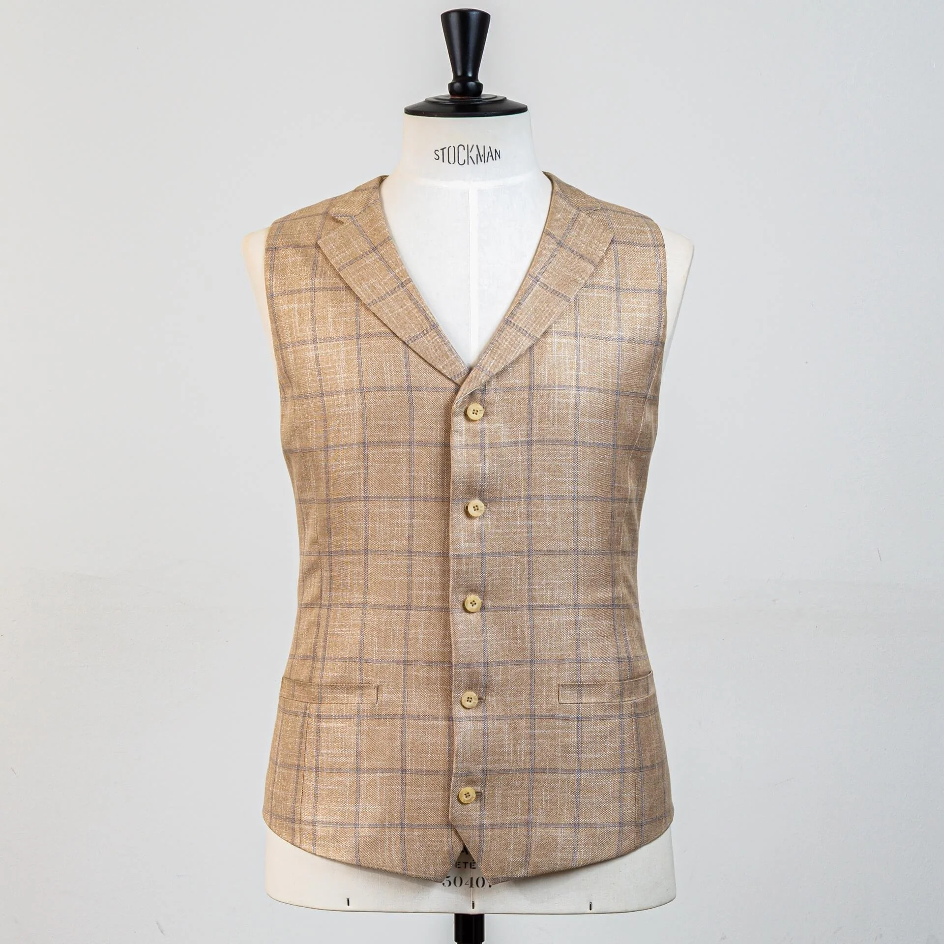 Volledig vooraanzicht zandkleurig bespoke gilet met subtiel blauw windowpane ruit. Single-breasted model met 5 hoornen knopen en notch revers, perfect bij groen trouwpak.