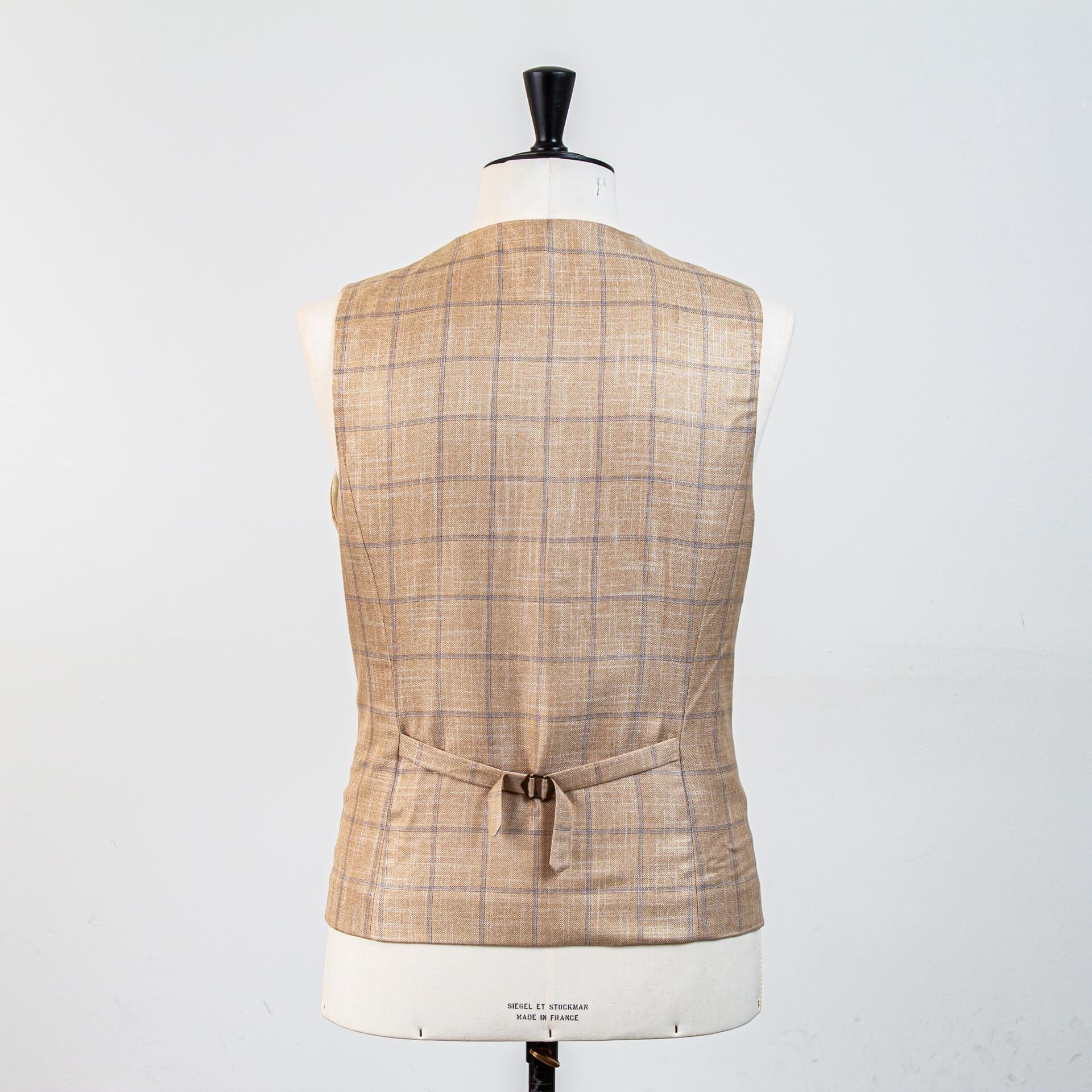 Achterzijde zandkleurig bespoke gilet volledig in stof met verstelbare rugband. Doorlopend ruitpatroon op rug, draagbaar als los kledingstuk na de bruiloft.