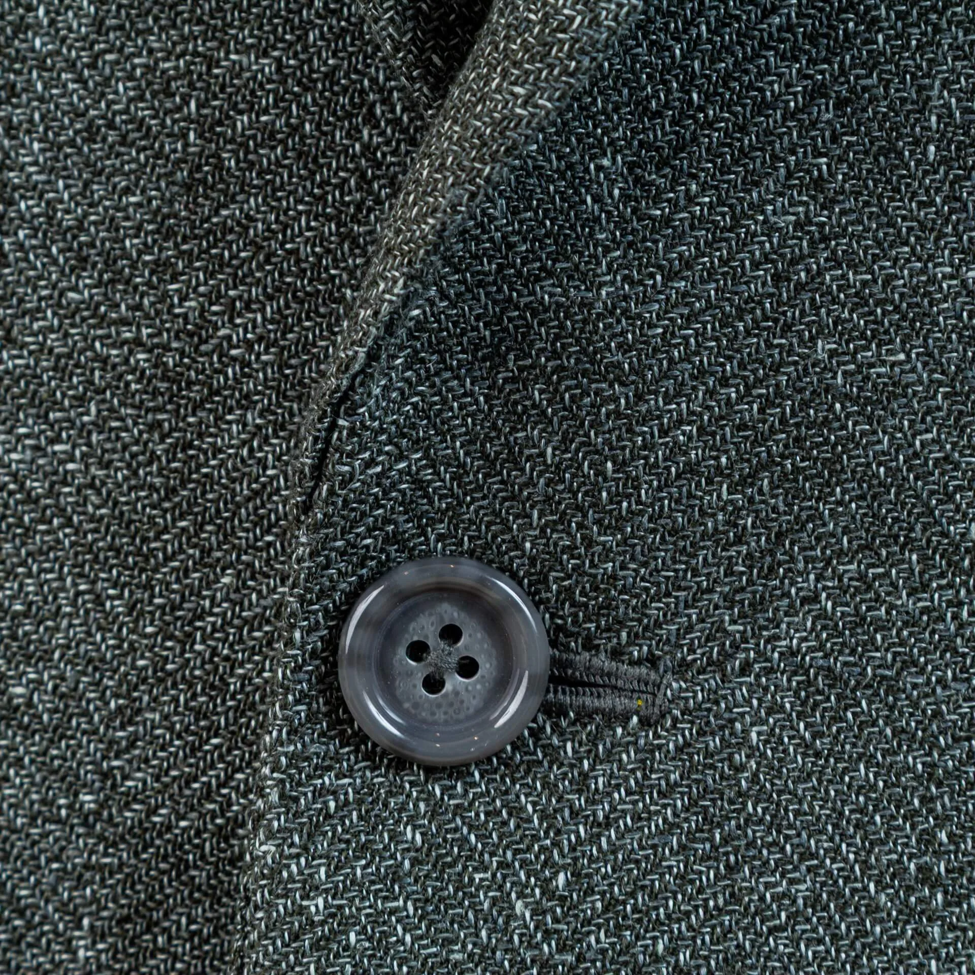 Detail frontknoop en handgemaakt knoopsgat van groen linnen trouwpak. Groene parelmoer knoop passend bij wol-linnen-zijde stof, met ambachtelijk knoopsgat.