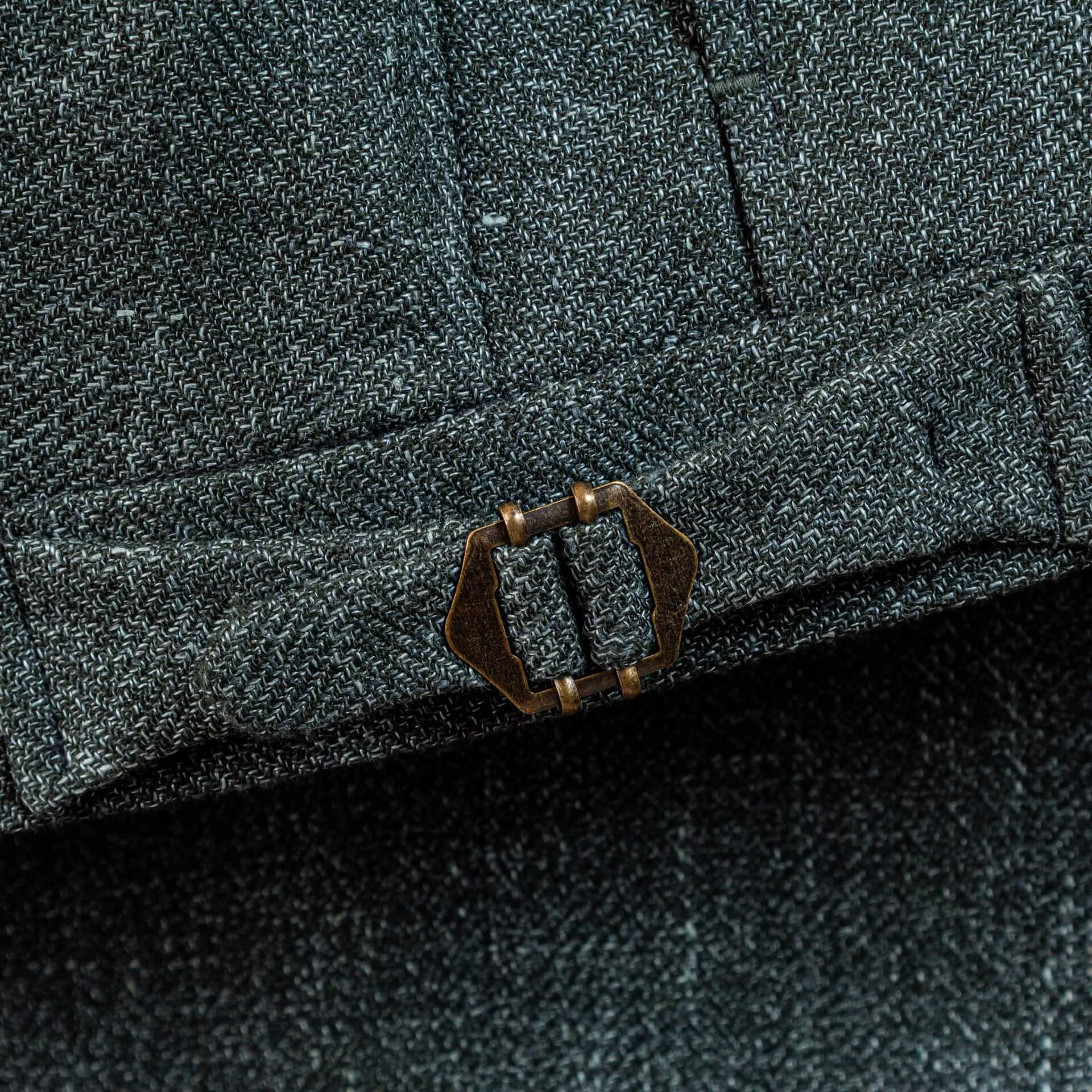 Close-up bronzen verstelgesp op groene trouwpantalon. Klassiek detail voor dragen zonder riem, onderdeel van bespoke trouwpak in wol-linnen-zijde blend.