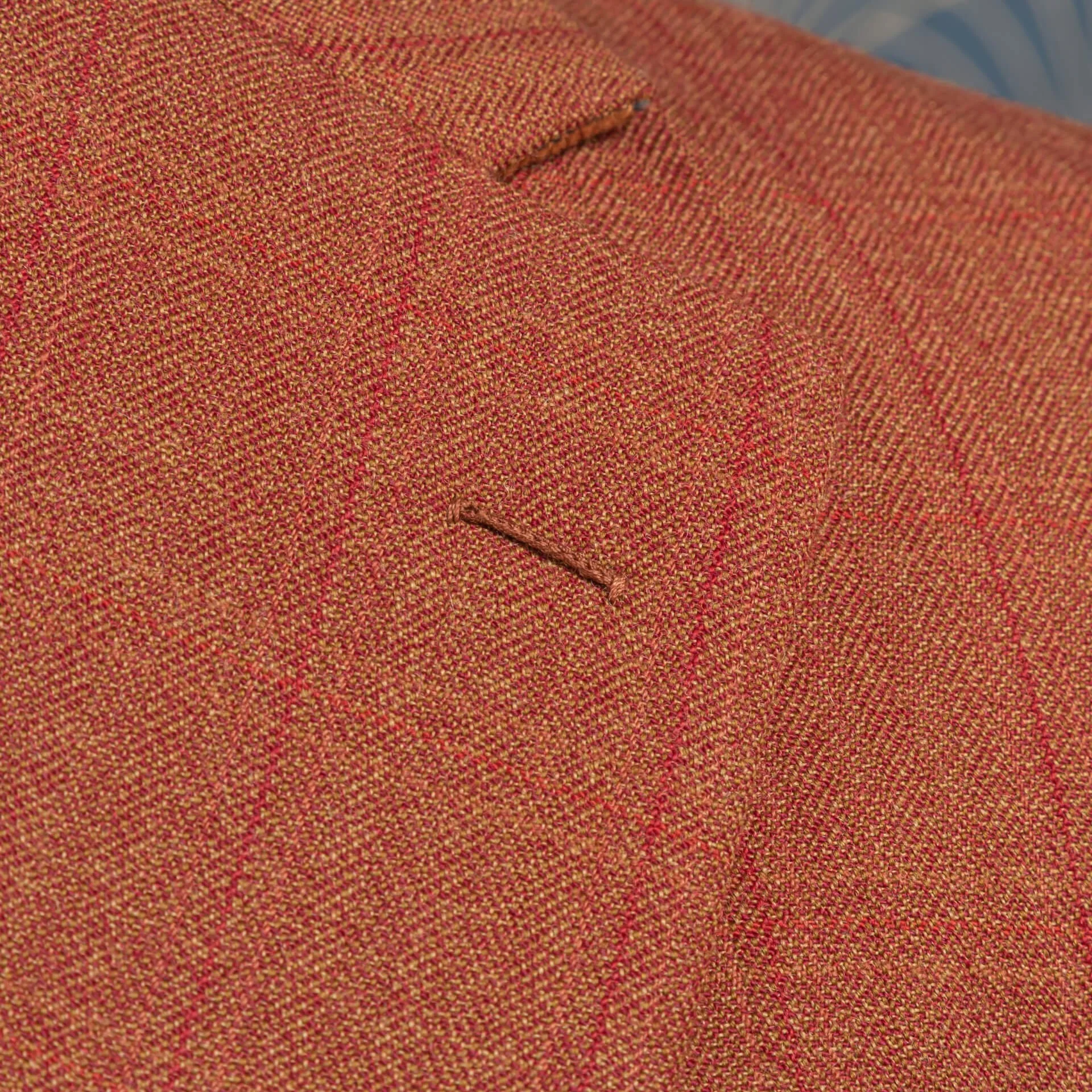 Close-up handgestikt flowerloop op burnt orange wol colbert, traditioneel bespoke tailoring detail