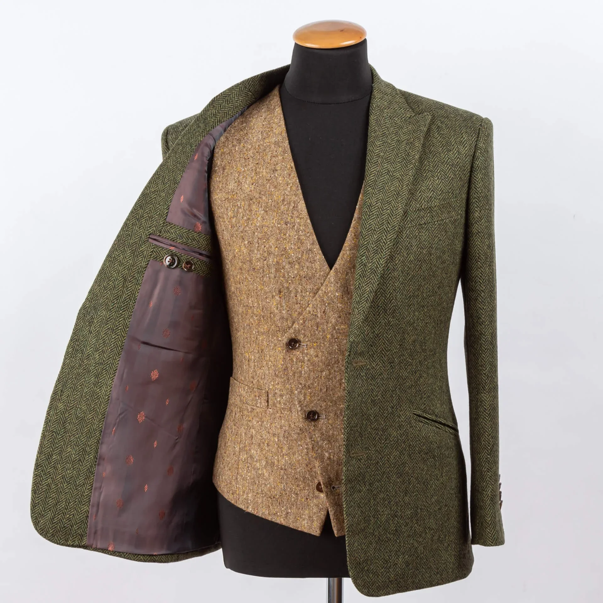 Olijfgroen tweed colbert geopend toont asymmetrisch goudbruin Donegal gilet en bordeaux voering met paisley patroon, volledige driedelige ensemble op kleermakersbust