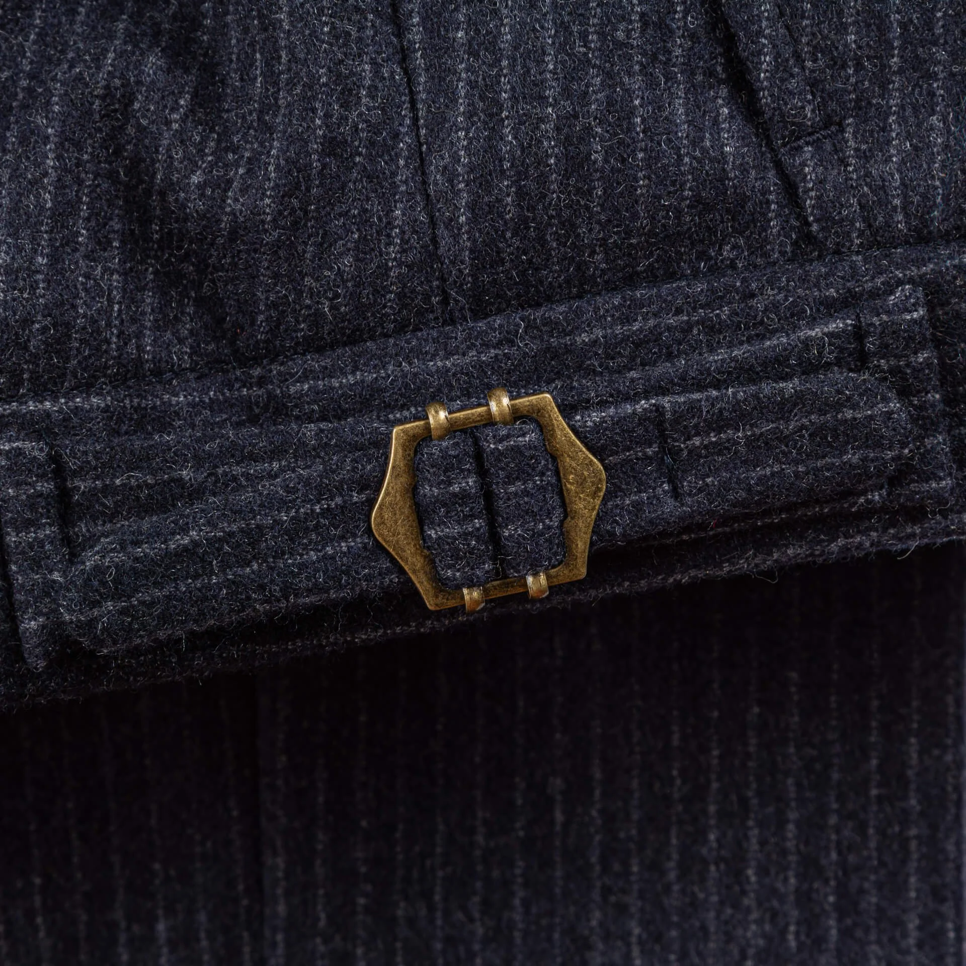 Extreme close-up van bronzen hexagonale buckle op navy pinstripe broekband, vintage Brits maatwerk detail voor verstelbare pasvorm