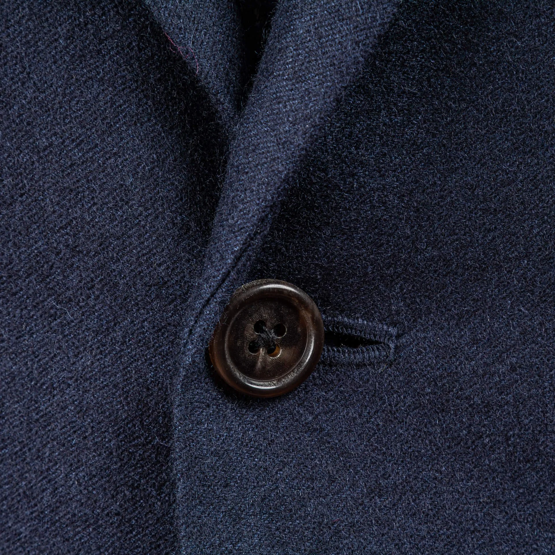 Close-up van hoornknoop op blue melange colbert, melange textuur en notch lapel detail zichtbaar