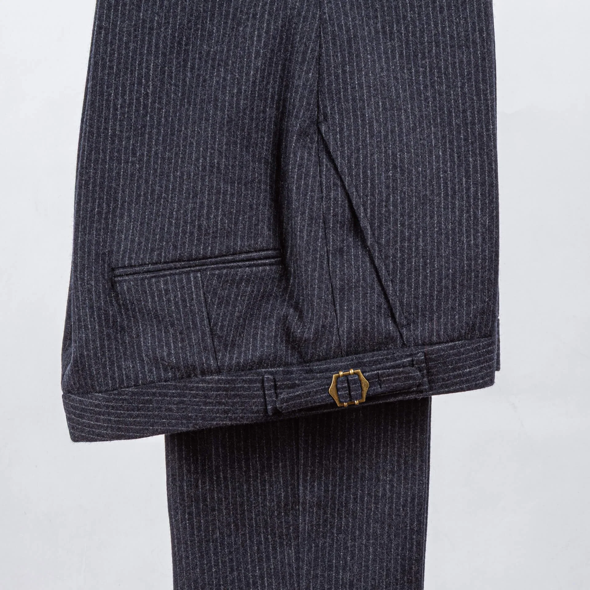 Navy pinstripe broek van Fox Brothers merinowol op houten hanger, detail van bronzen hexagonale buckle op broekband, maatwerk trouwpak