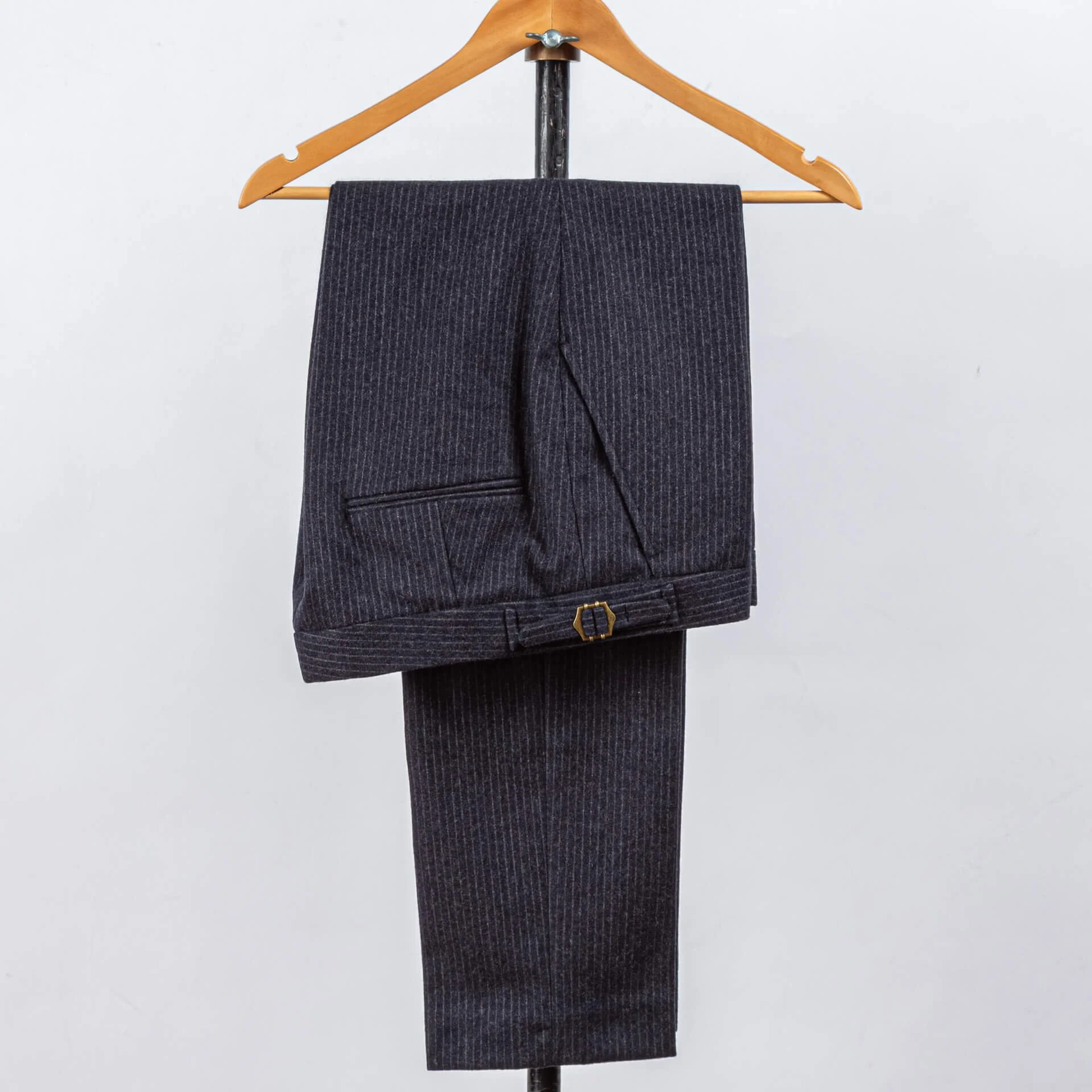 Navy pinstripe broek van Fox Brothers merinowol op houten hanger, detail van bronzen hexagonale buckle op broekband, maatwerk trouwpak