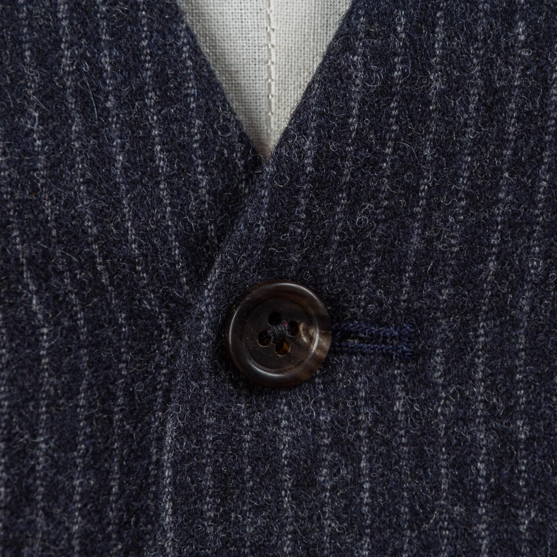 Close-up van donkere hoornknoop op navy pinstripe gilet, textuur van Fox Brothers merinowol met verticale krijtstreep zichtbaar
