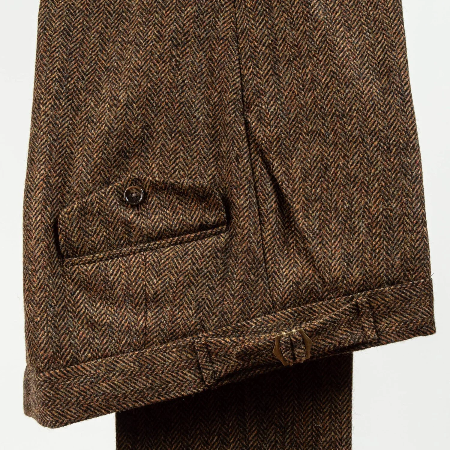 Close-up van klepzak met knoop op brown herringbone tweed broek, klassiek vintage detail, 340 gram lamswol, handwerk maatbroek