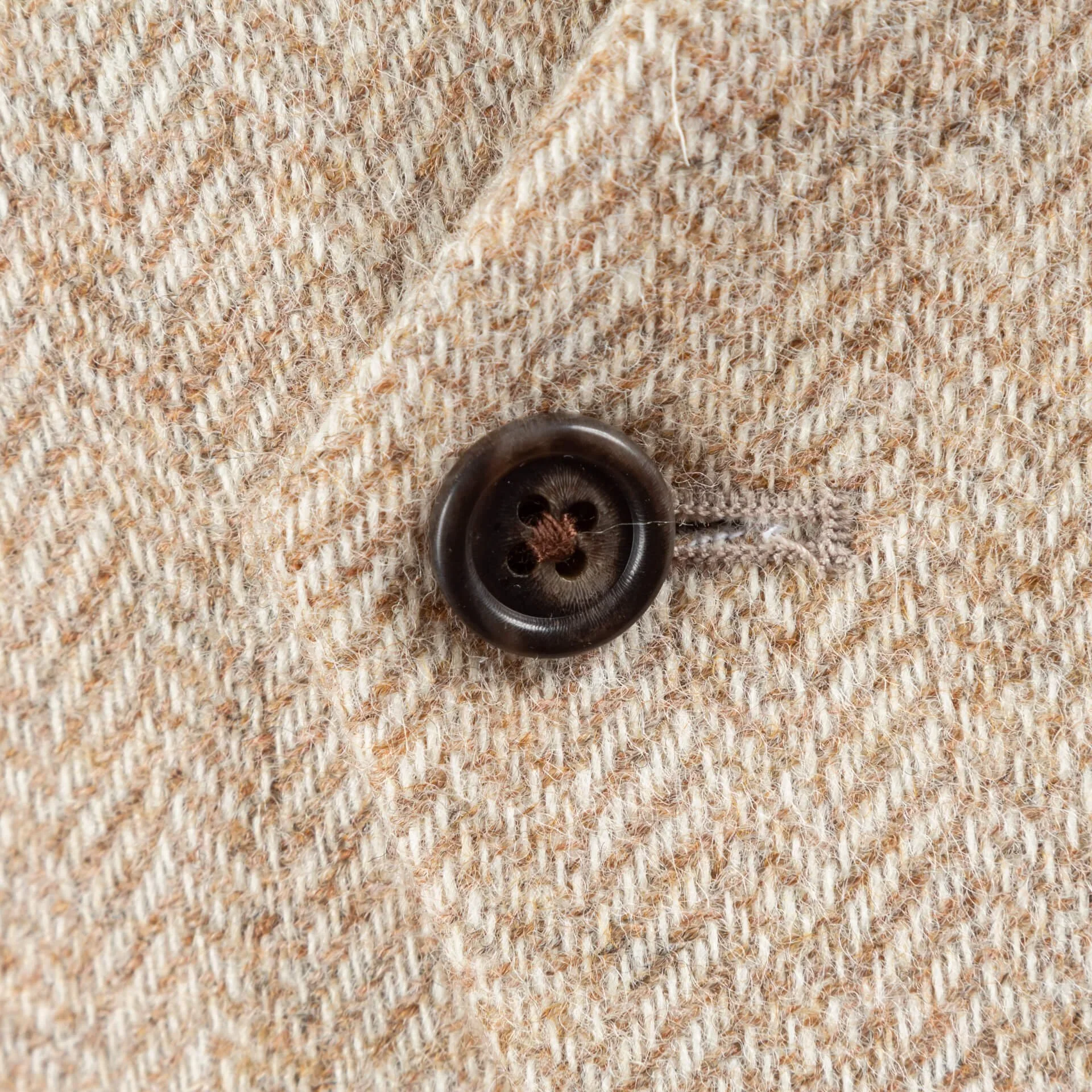 Bruine hoornen knoop op light sand herringbone tweed, visgraatpatroon zichtbaar