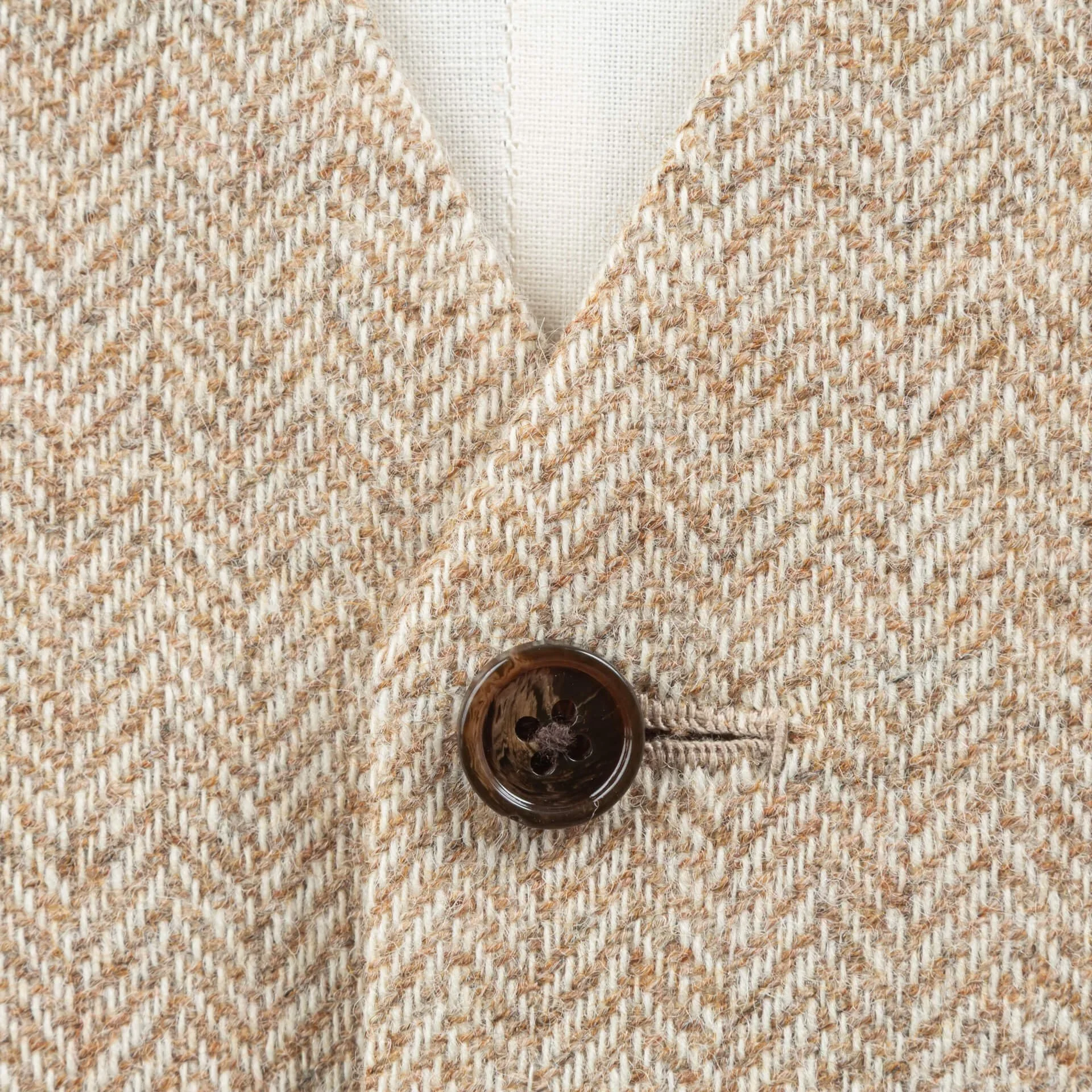 Macro-opname van light sand herringbone tweed stof met donkerbruine hoornen knoop, toont het karakteristieke visgraatpatroon van Holland en Sherry Sherry Tweed