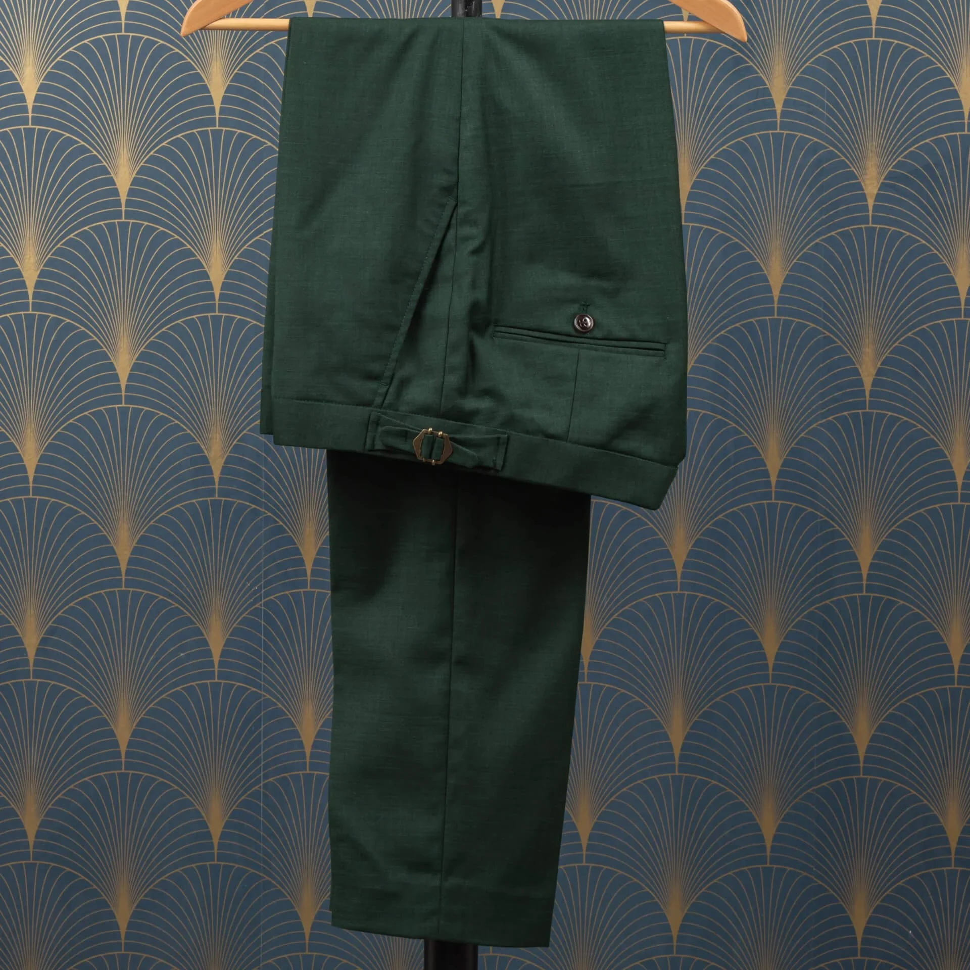 Op maat gemaakte pantalon in saffiergroene merino wol sharkskin met koperen side adjusters en klepzak met knoop, hangend aan houten hanger