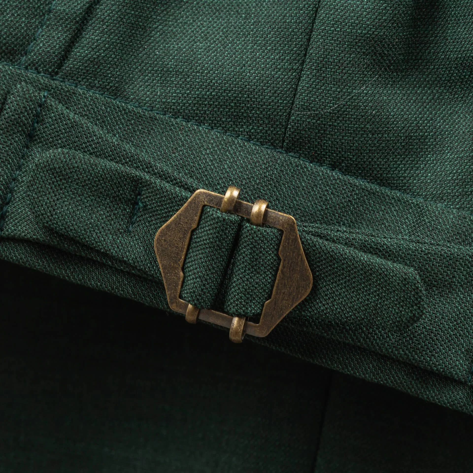 Macro-opname van koperen side adjuster gesp op saffiergroene merino wol pantalon, klassieke tailleband-verstelling zonder riem