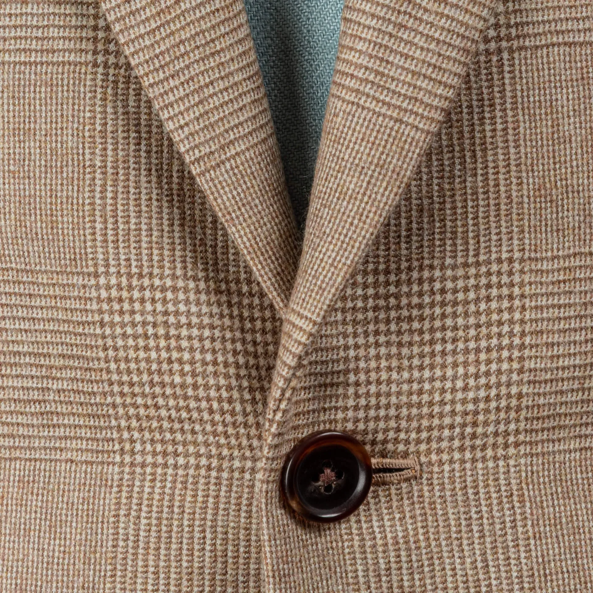 Close-up van bruine hoornen knoop met handgestikt knoopsgat op camel check flannel colbert