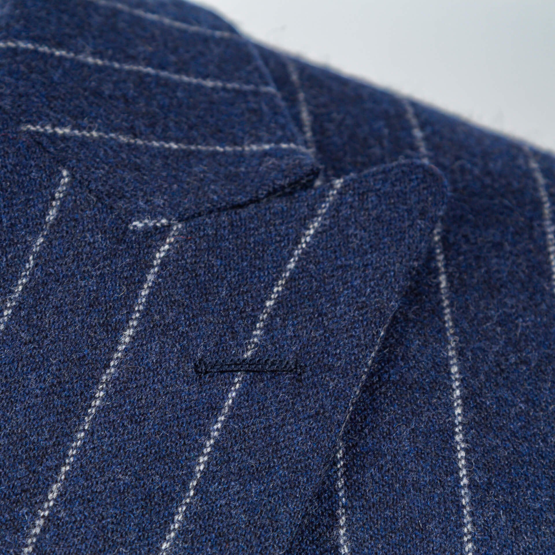 Close-up van peak lapel met handgestikt flowerloop op navy krijtstreep flannel colbert
