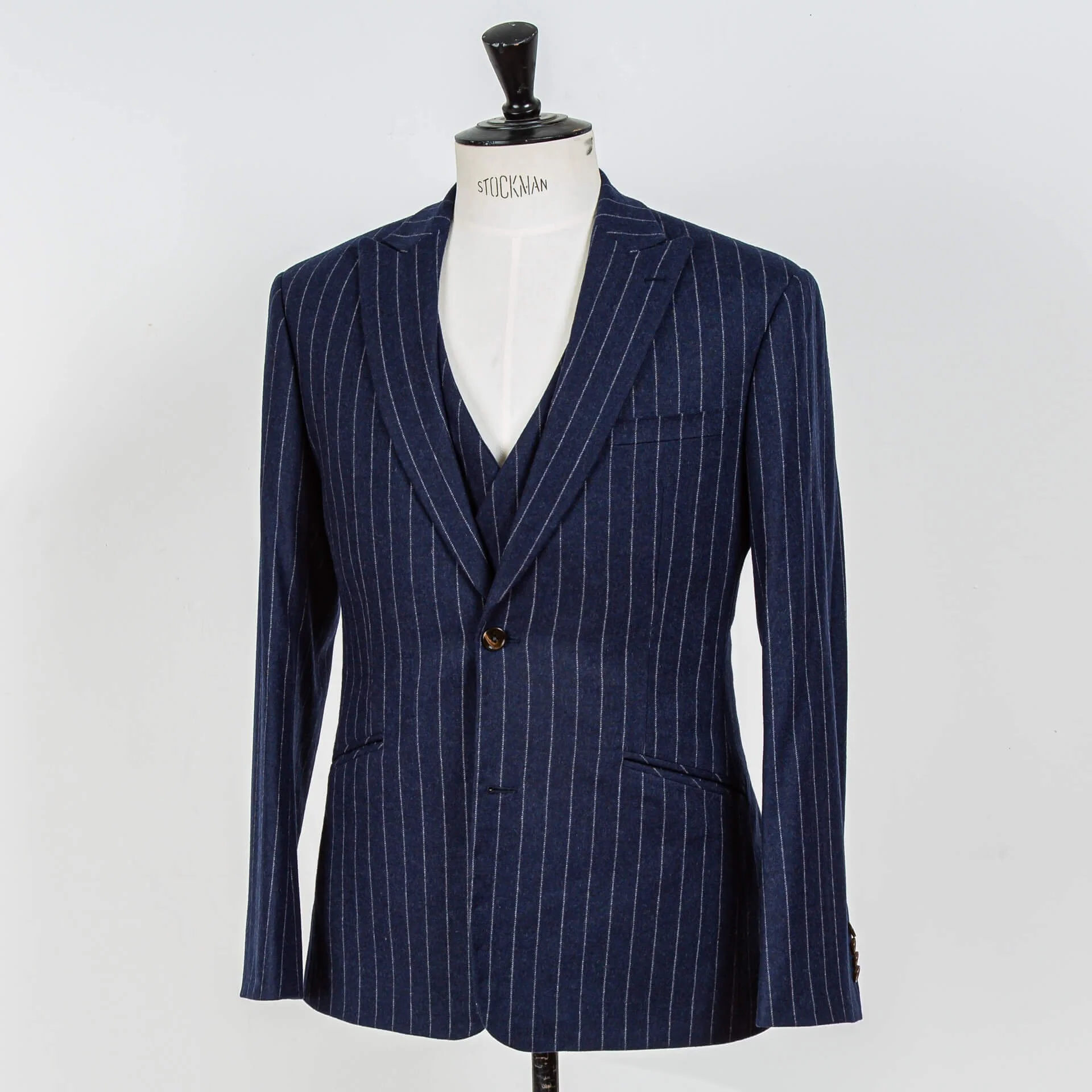 Navy krijtstreep maatpak in flannel met peak lapels en schuine paspelzakken, driekwart aanzicht toont silhouet en mouwknopen