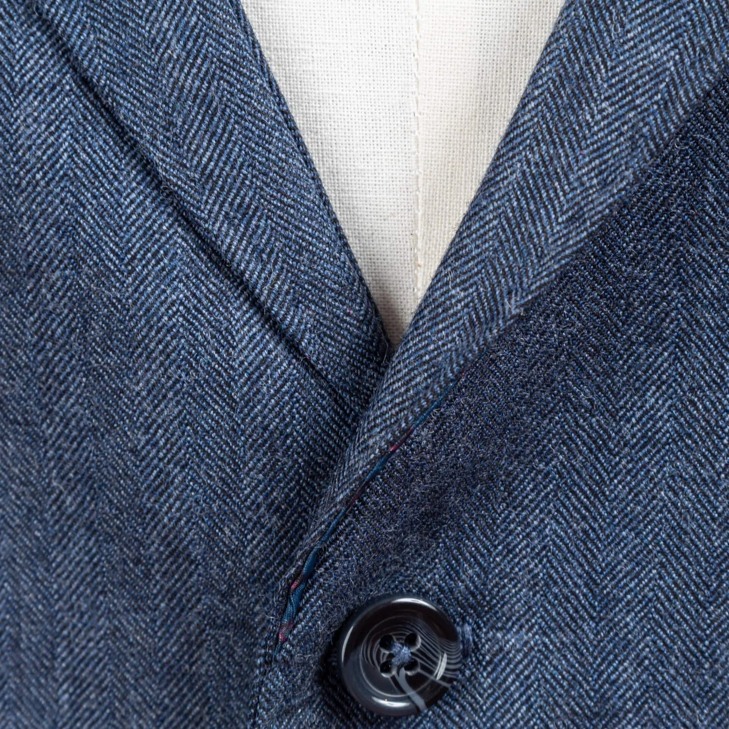 Close-up van bovenste hoornen knoop met revers op denim blauw herringbone gilet