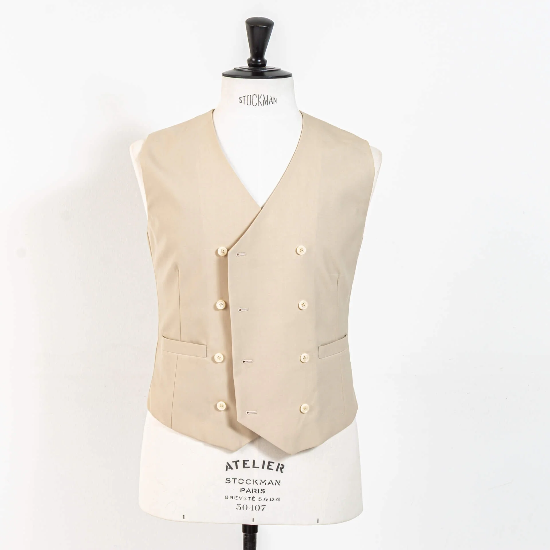 Double-breasted gilet op maat in biscuit kleurige wol van Bateman & Ogden, 4x2 model zonder revers met paspelzakken en crème knopen, gepresenteerd op Stockman paspop