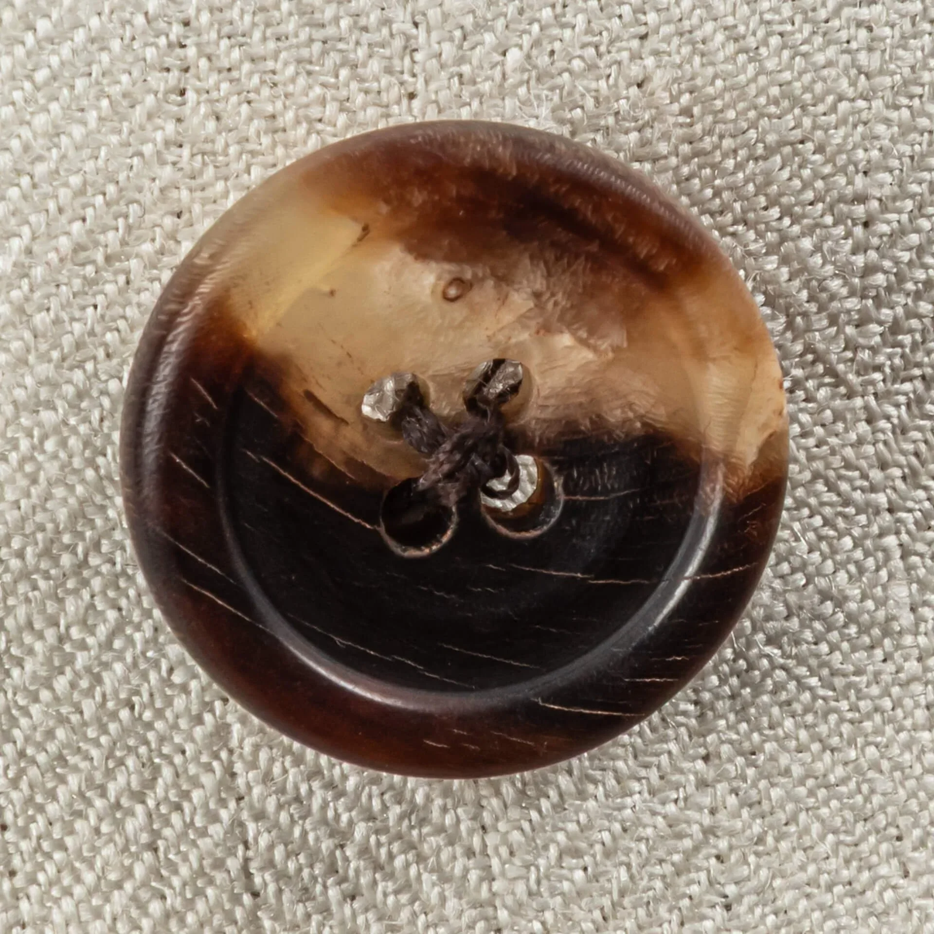 Extreme close-up van een donkerbruine hoornen knoop met natuurlijke nerf, gebruikt op een off-white double-breasted trouwpak.