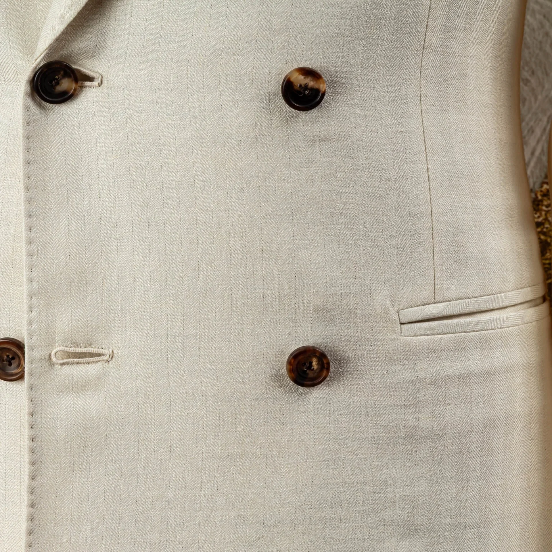 Detail van het voorpand met hoornen knopen, knoopsgaten en paspelzakken op een off-white double-breasted trouwpak in wol-linnen-zijde.