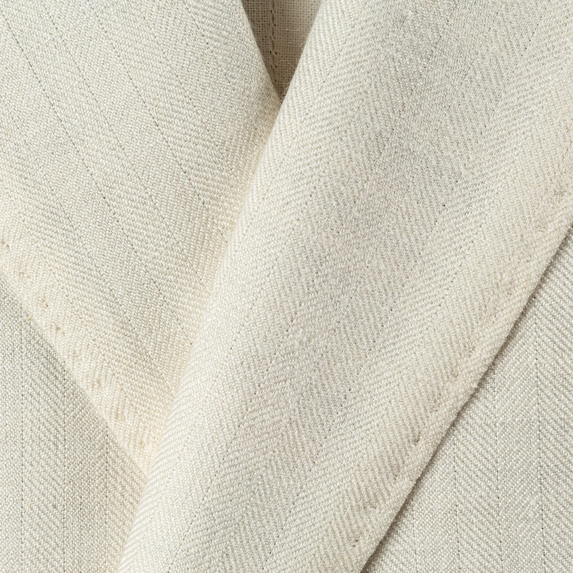 Close-up van het herringbone weefsel van de wol-linnen-zijde blend van Caccioppoli op de revers van een off-white trouwpak.
