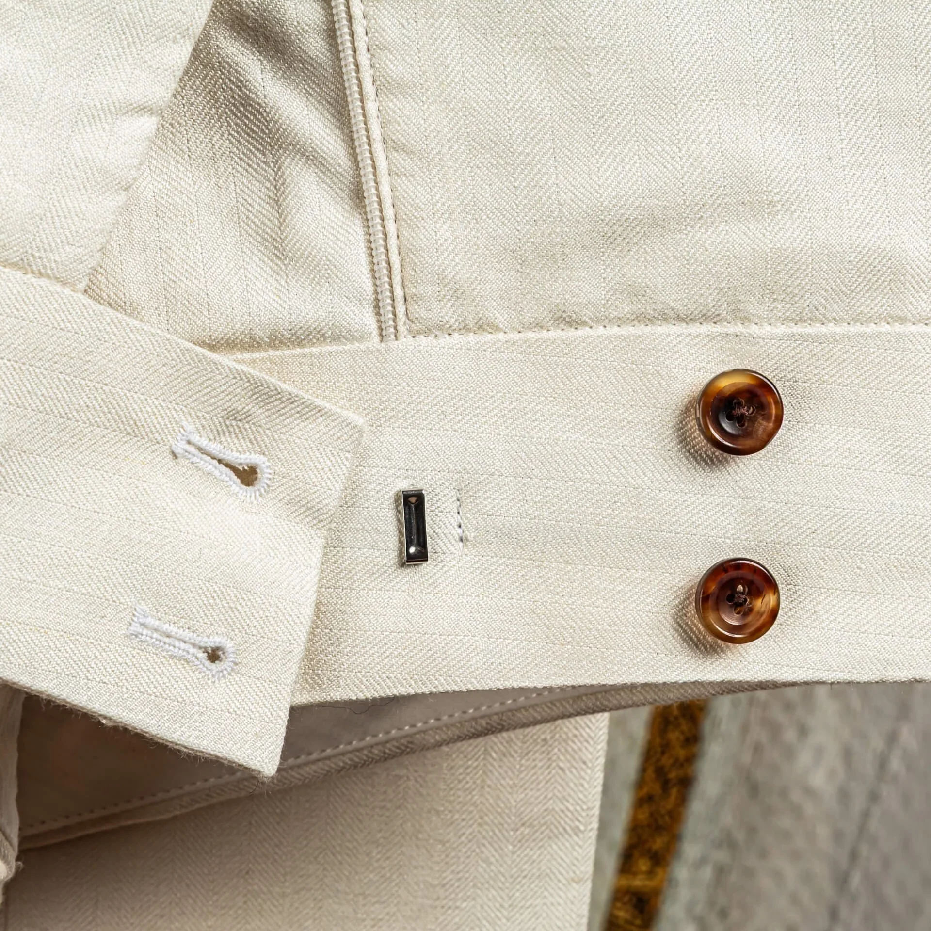 Detail van de dubbele knoopsluiting op de broekband van een off-white pantalon in wol-linnen-zijde.