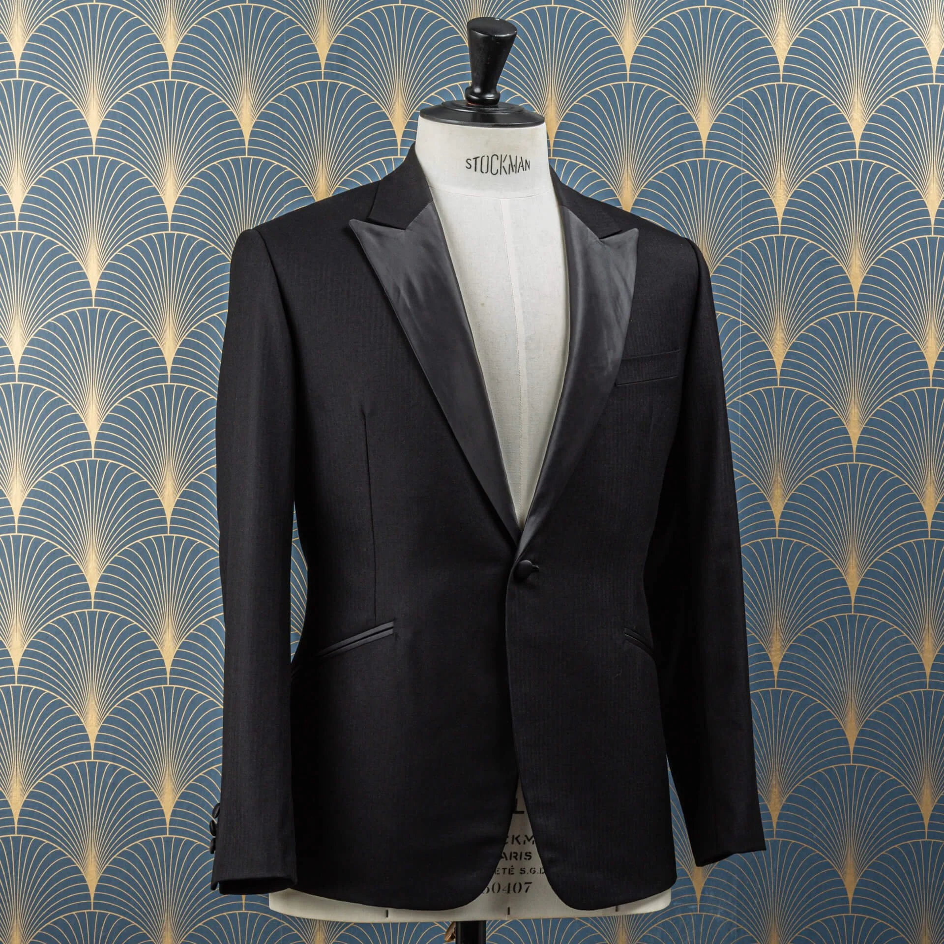 Zijaanzicht van de jas van een smoking voor het trouwen op maat in zwarte visgraat met peak lapels, schuin geplaatste zakken en met stof beklede mouwknopen, Super 100's wol en cashmere Holland & Sherry Cape Horn