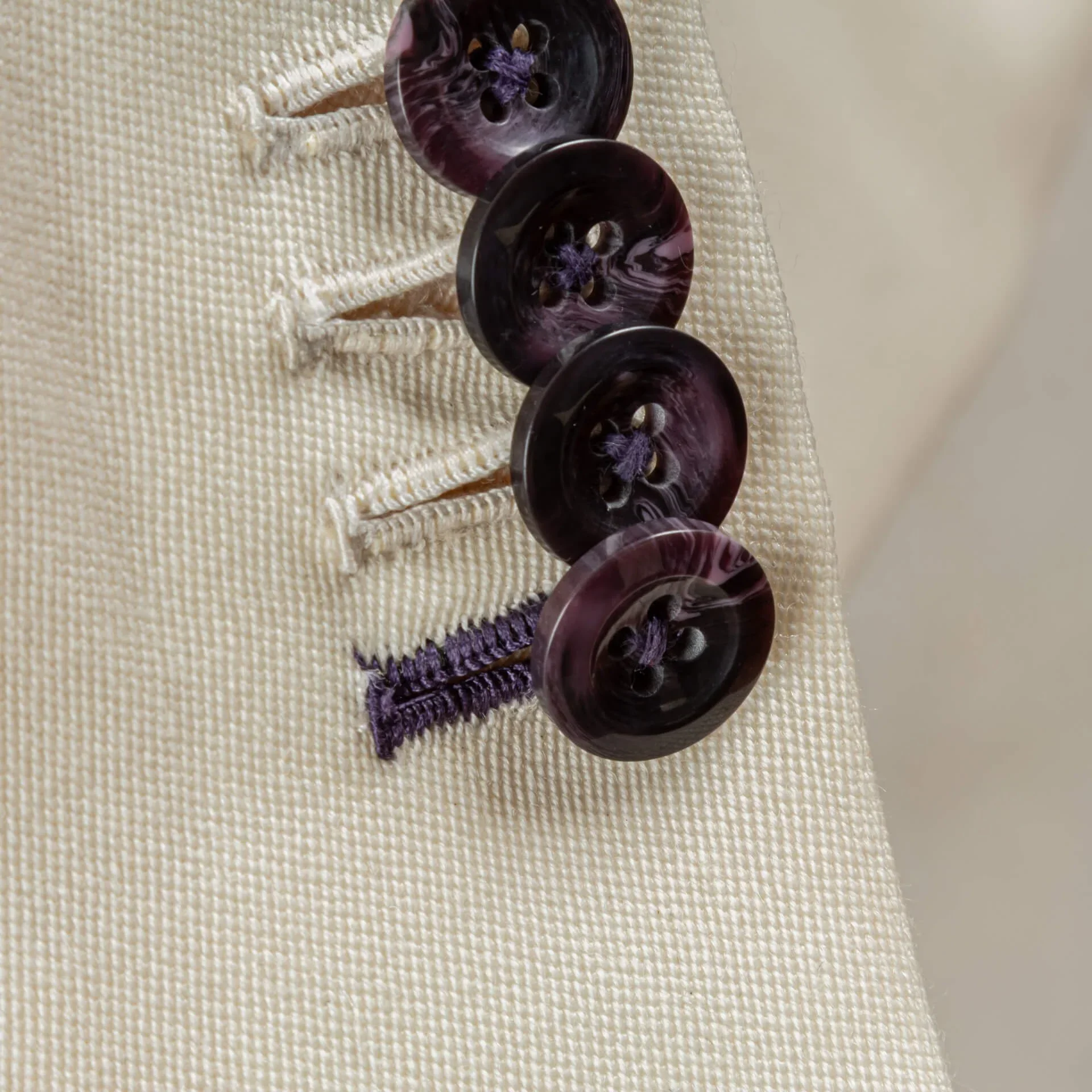Close-up van vier mouwknopen met paarse nerf en handgemaakt paars knoopsgat op witte barathea-weving van een double-breasted jasje, trouwpak op maat in Holland & Sherry Black Tie barathea van 370 gram