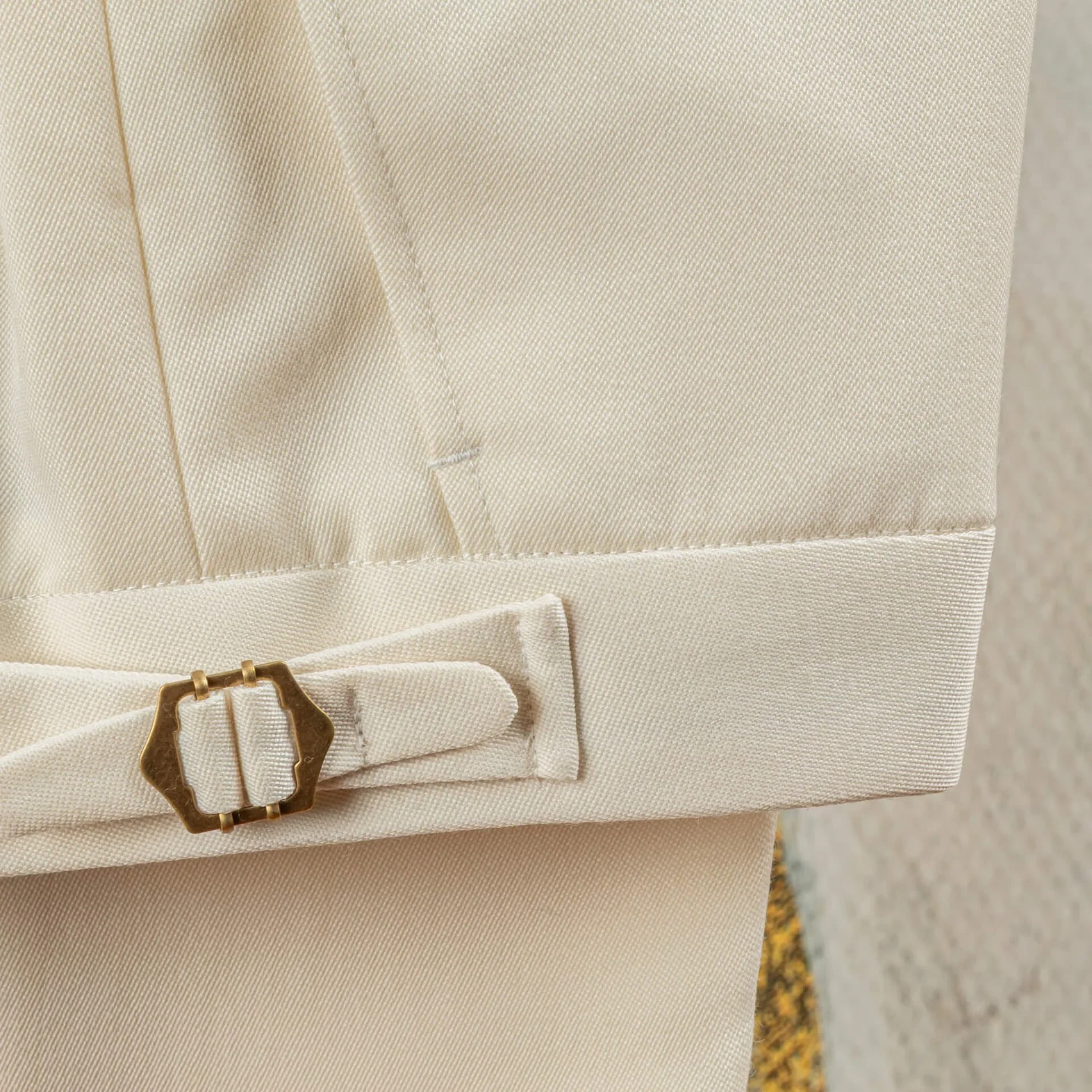 Close-up van een zijspanner met goudkleurige buckle op de tailleband van een witte pantalon in barathea, trouwpak op maat in Holland & Sherry Black Tie barathea van 370 gram