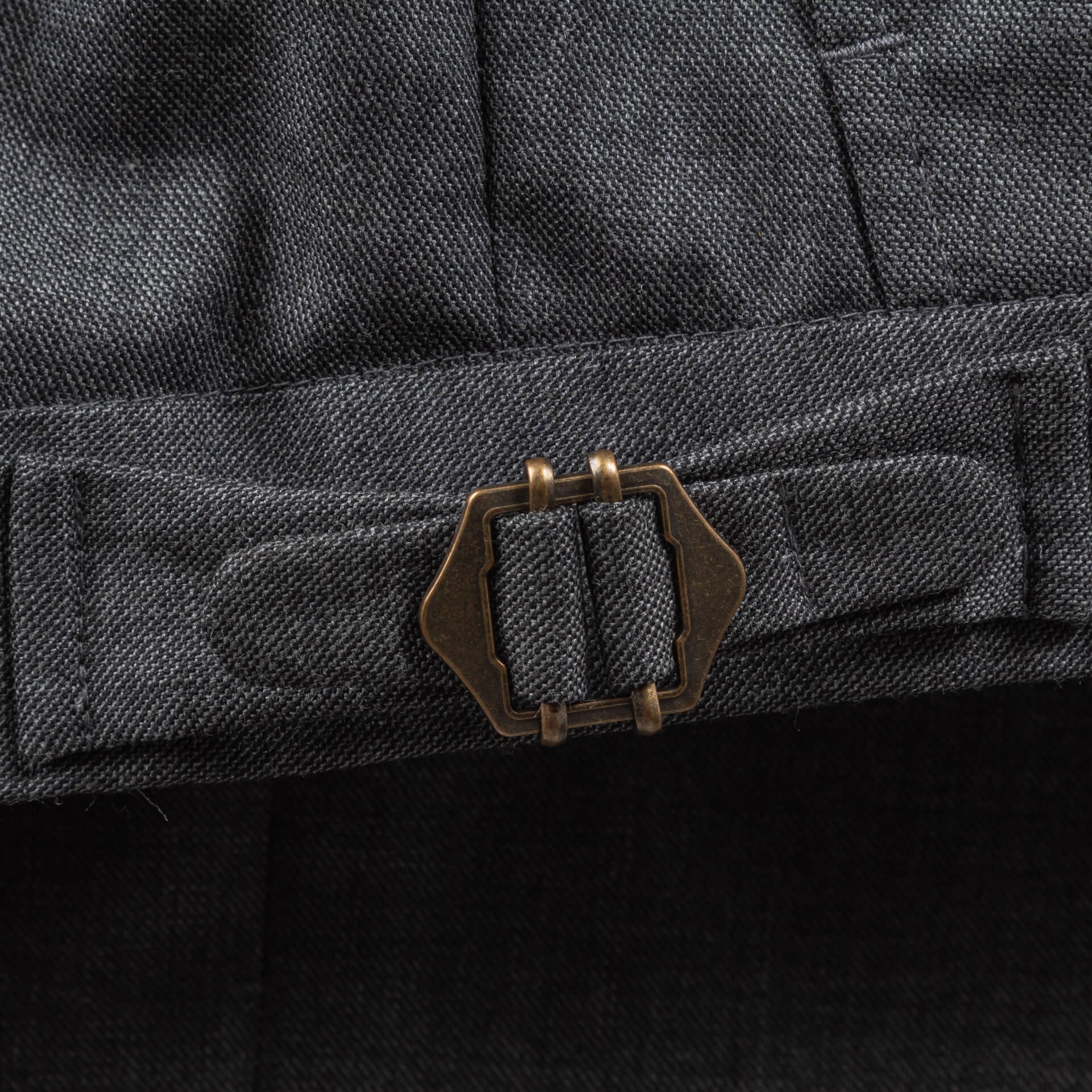 Zijtrekker van brons kleurig metaal op de broekband van een grijze sharkskin pak broek