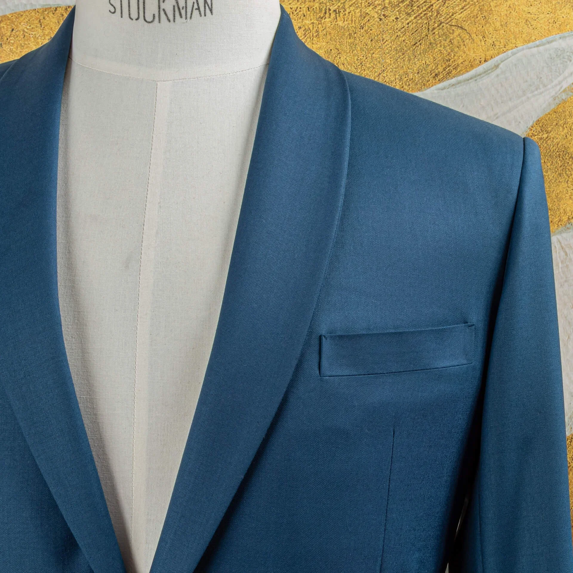 Close-up van shawl collar en paspelzak op bespoke petrol blauw colbert, toont verfijnd handwerk