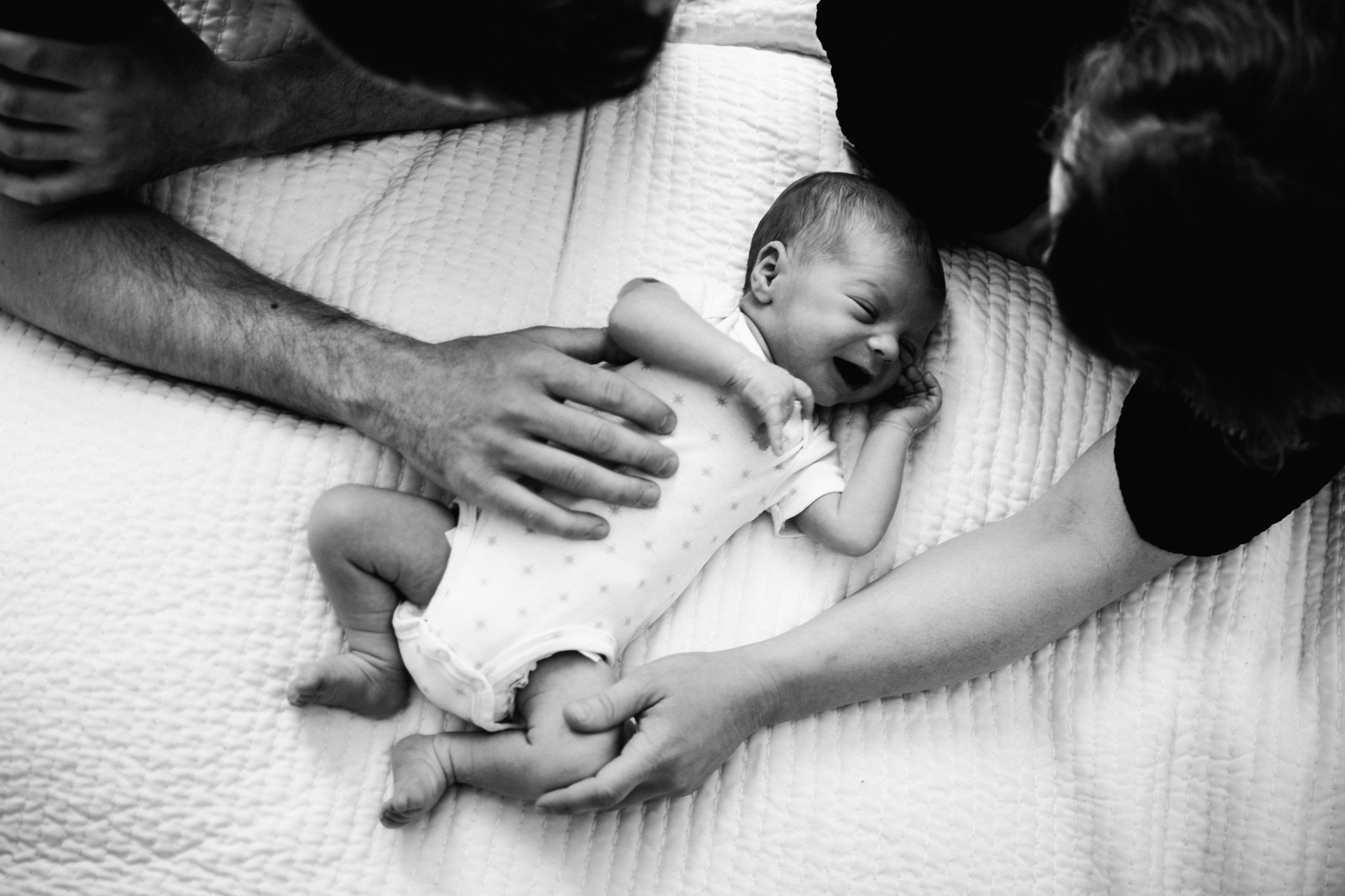 photo-dun-nouveau-ne-couche-sur-le-dos-sur-un-lit-encadre-de-ses-parents-photographe-famille-montreal.jpg