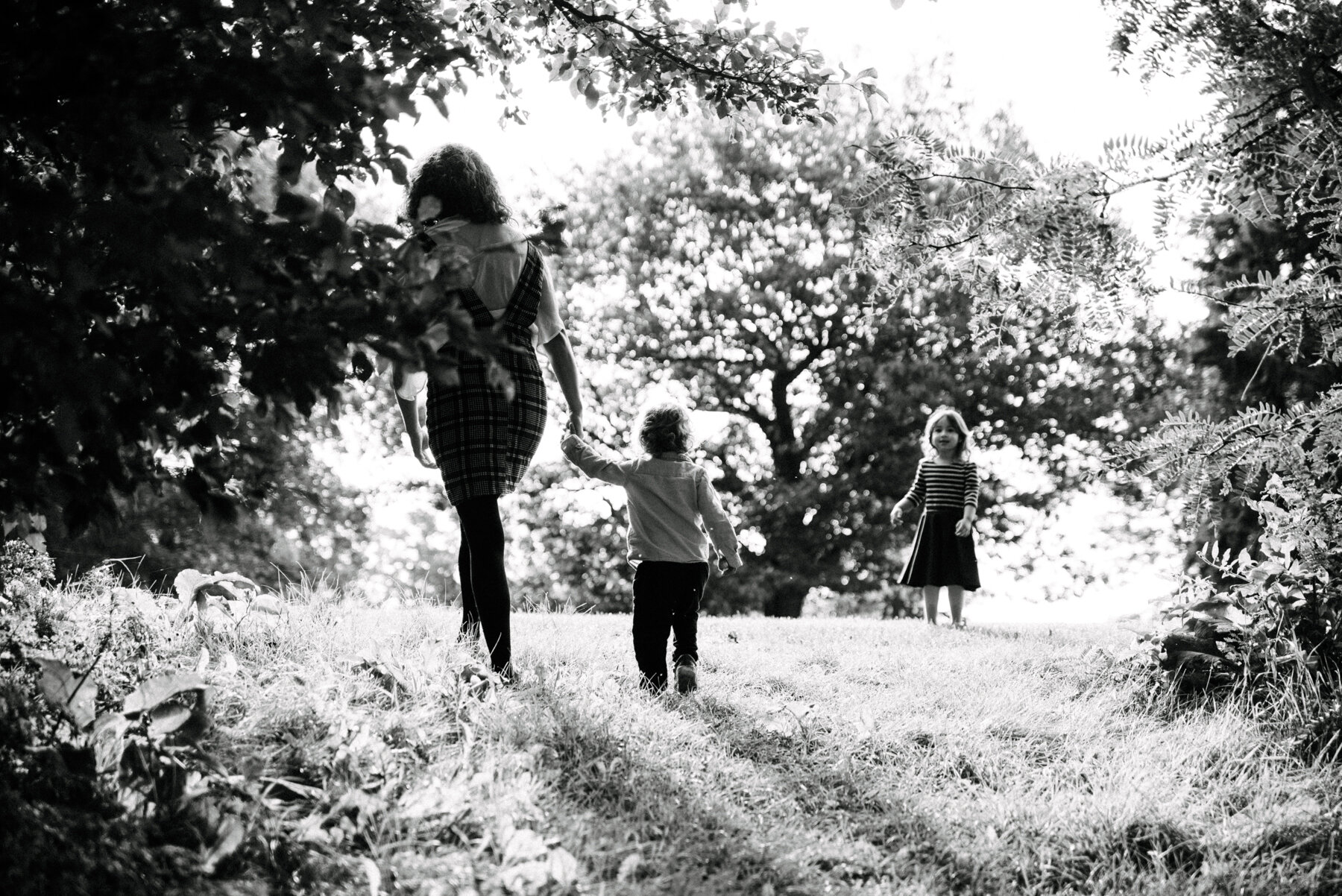 047photo-noir-et-blanc-maman-qui-guide-ses-enfants-vers-une-clairiere-lumineuse-parc-maisonneuve-photographe-de-famille-a-montreal-marianne-charland-373.jpg