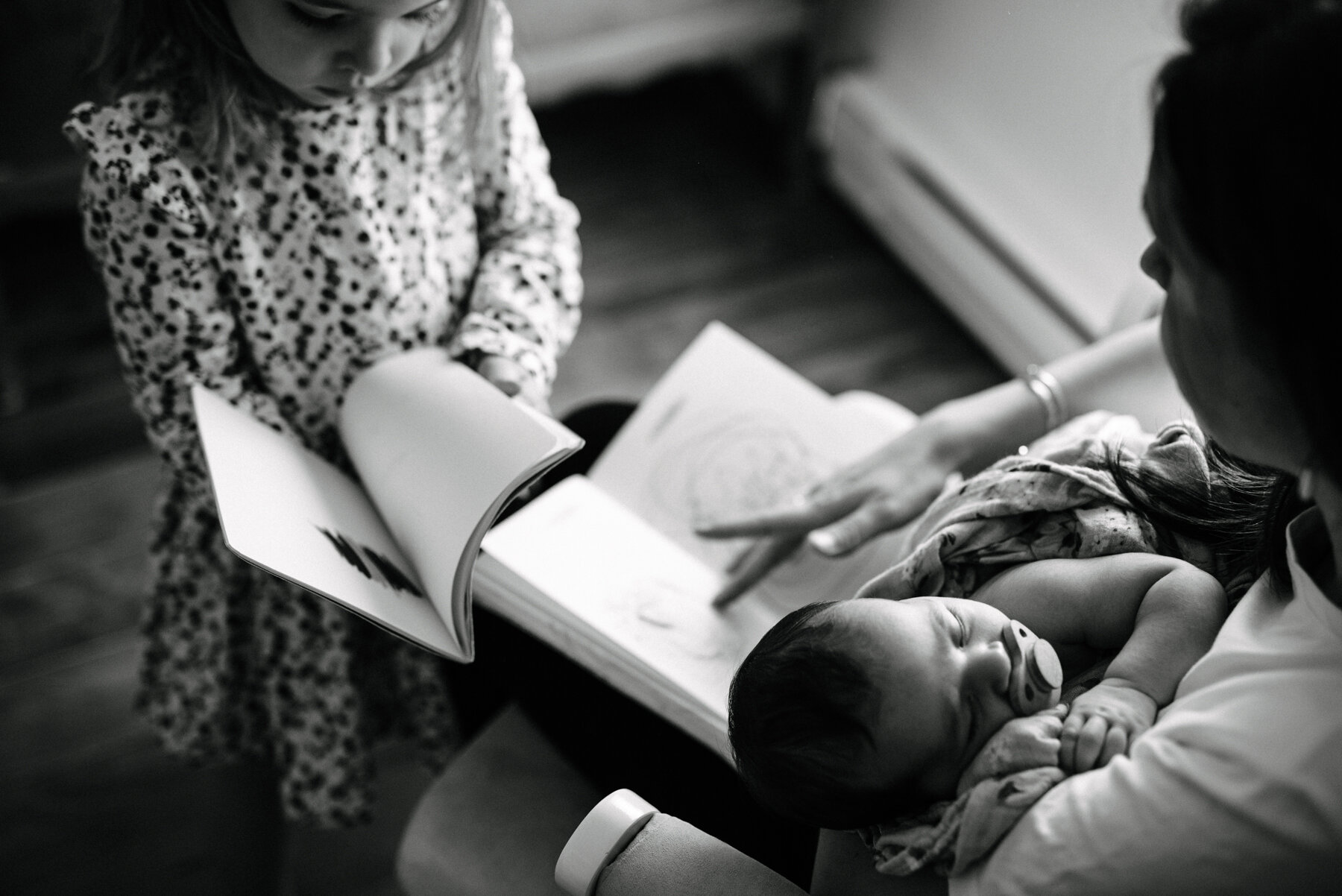 055photo-noir-et-blanc-mere-qui-regarde-un-livre-avec-sa-grande-en-tenant-son-bebe-photographe-de-famille-a-montreal-marianne-charland-397.jpg