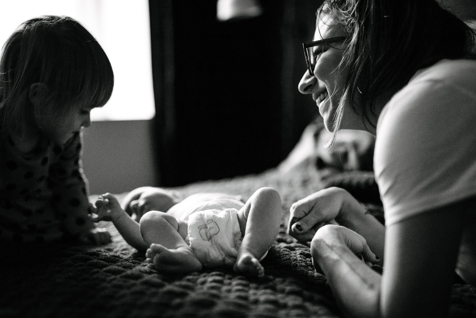 009photo-noir-et-blanc-maman-et-bebe-avec-grande-soeur-souriantes-sur-lit-photographe-lifestyle-de-maternite-a-montreal-marianne-charland-144.jpg