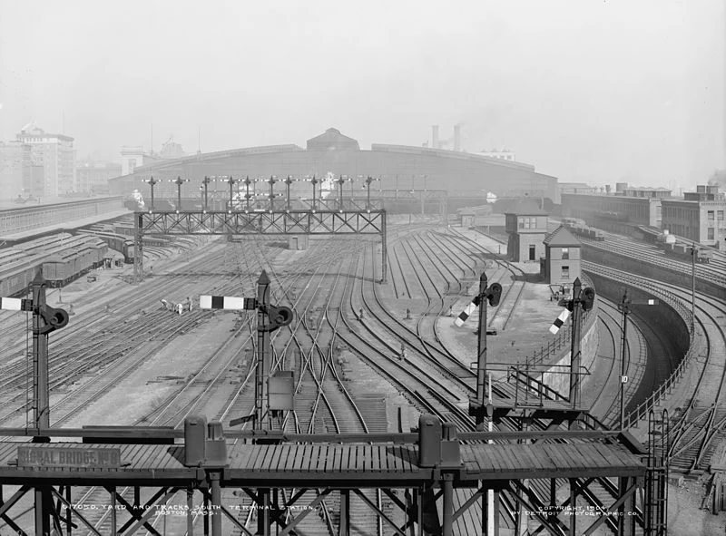 For location of the new site, the company decided on a $9 million, 35-acre expanse adjacent to Fort Point Channel, which was also the site of the New England Railroad terminal. Image: "Approach tracks and trainshed of South Station in Boston, Massachusetts in 1904", Detroit Photographic Co.