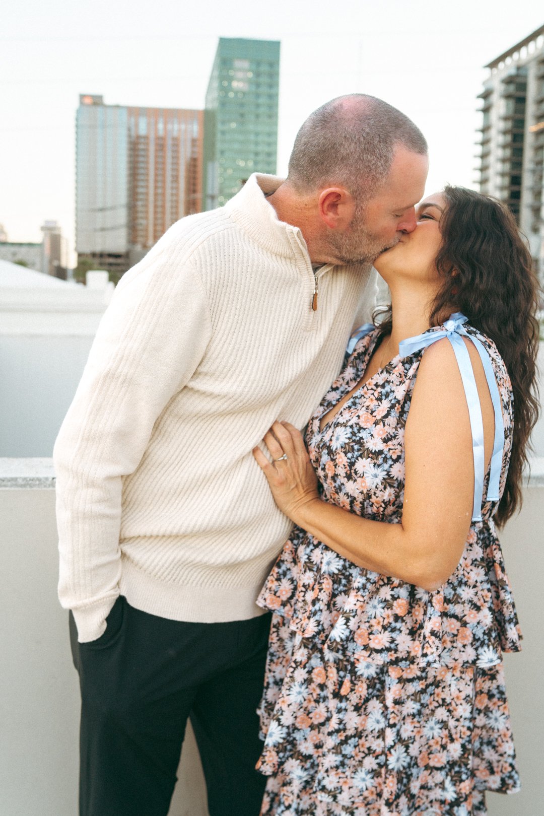A couple sharing a kiss on a rooftop with city buildings in the background.